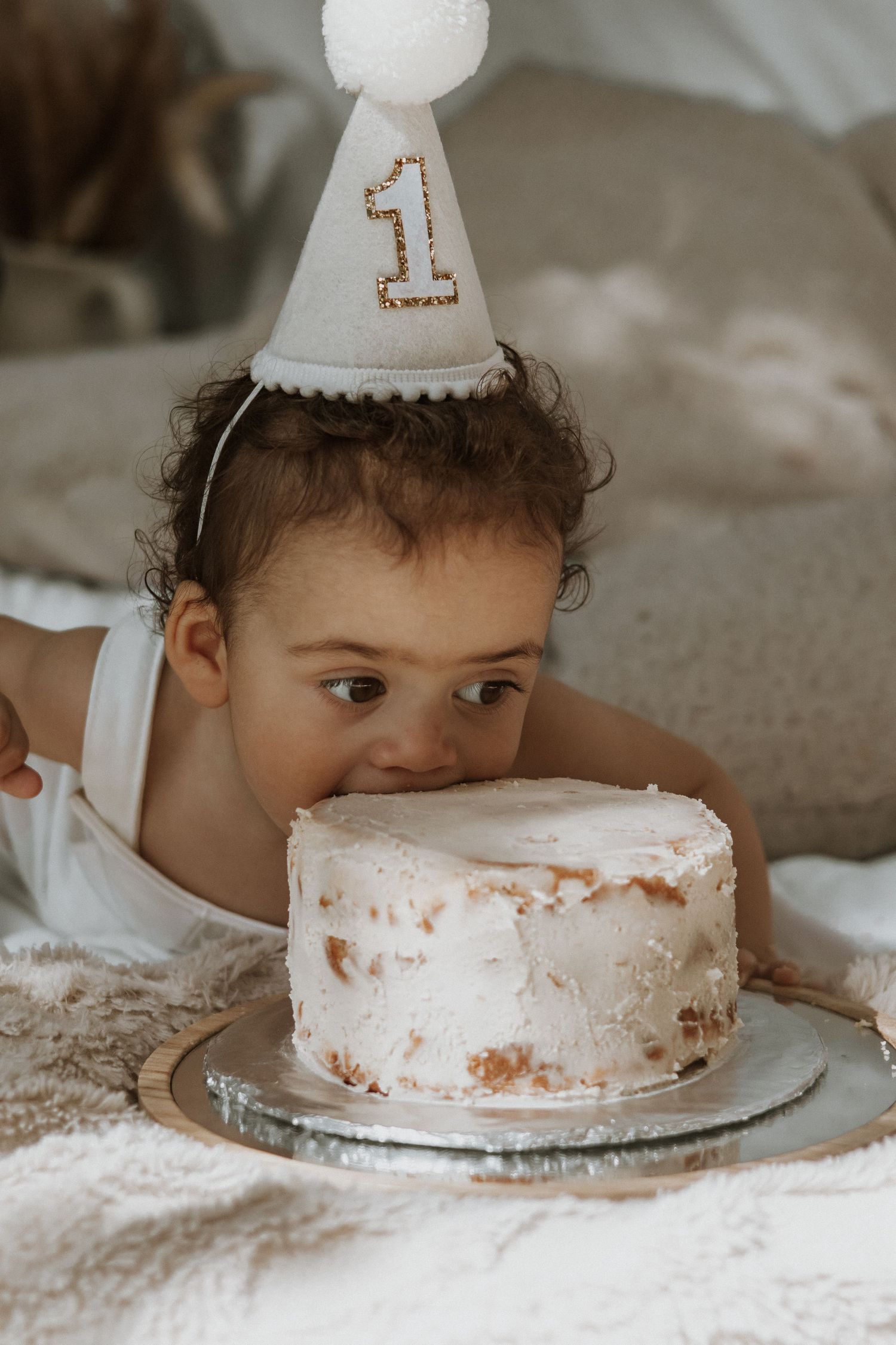 White birthday cake with number one party hat in soft neutral tones.
