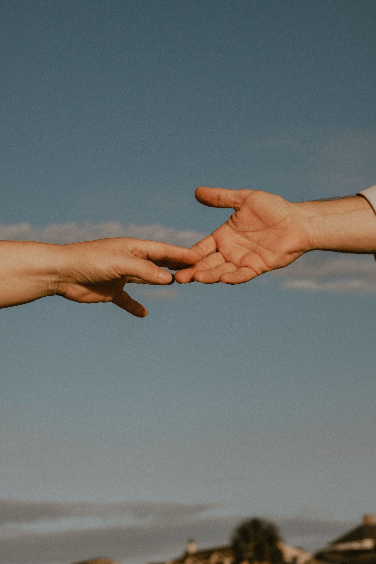 Two hands reaching toward each other against blue sky in symbolic connection.