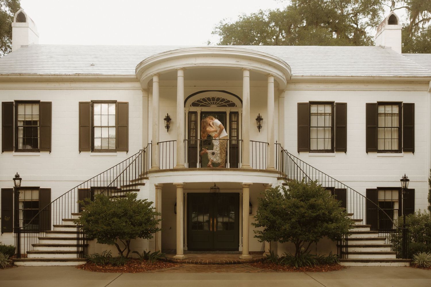 Elegant white Southern colonial mansion with dual staircases, black shutters, and a grand circular portico entrance.