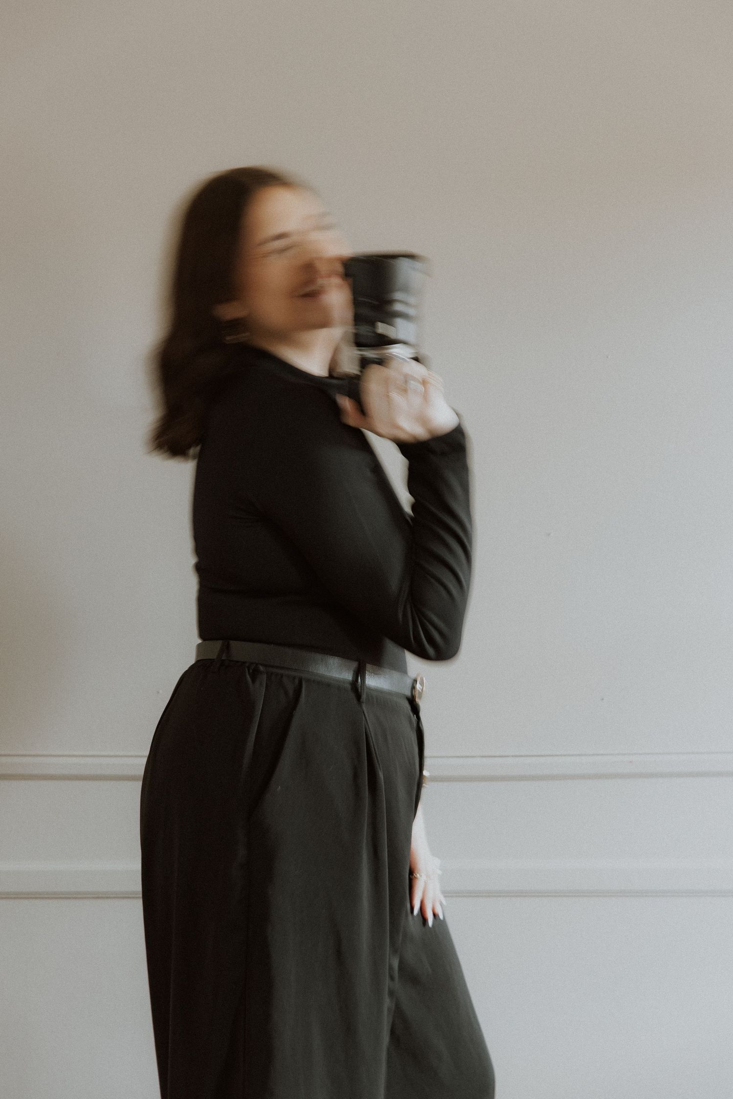 Motion blur portrait in black outfit against white wall.