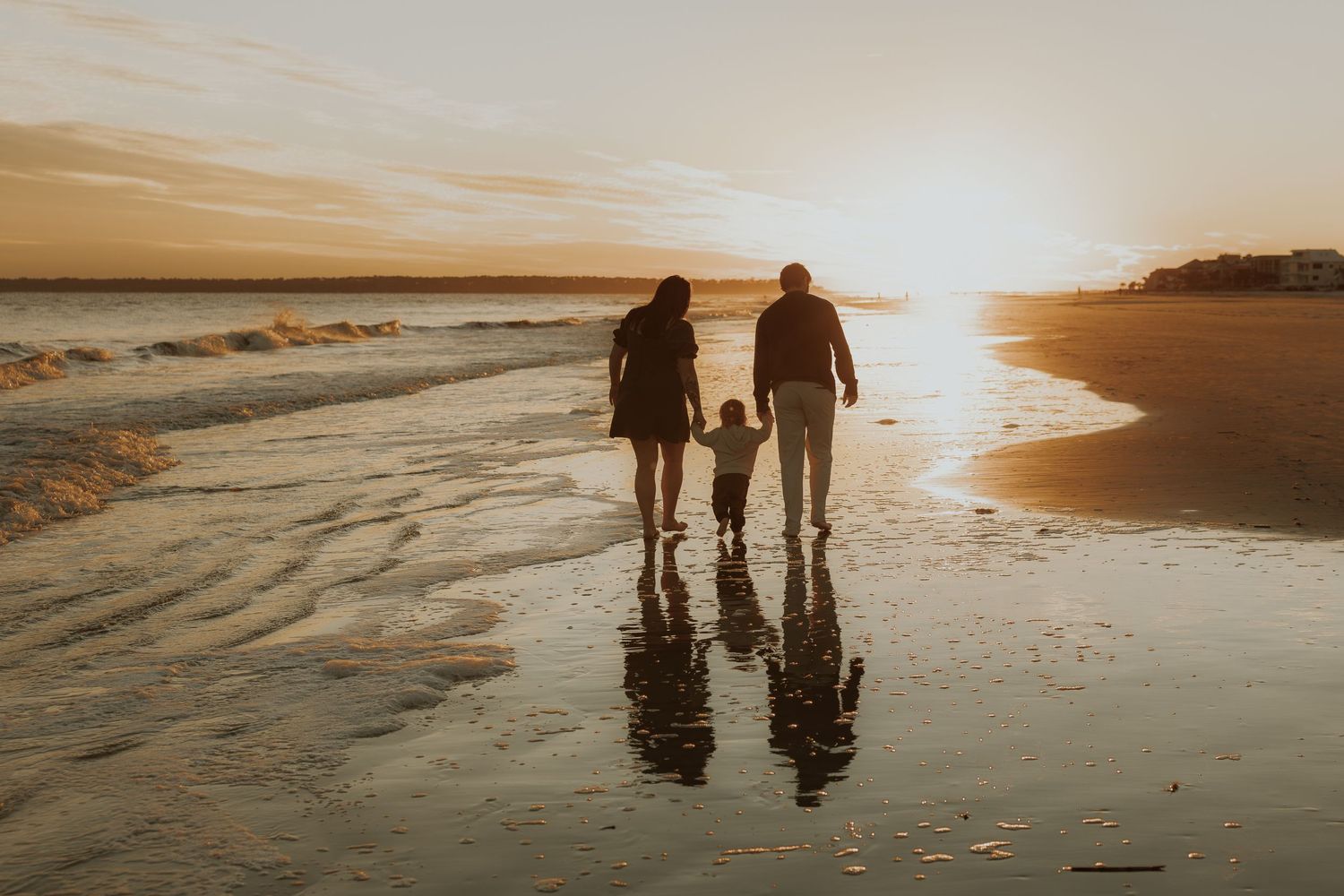 Two silhouettes walking on a beach at sunset with reflections in the wet sand.