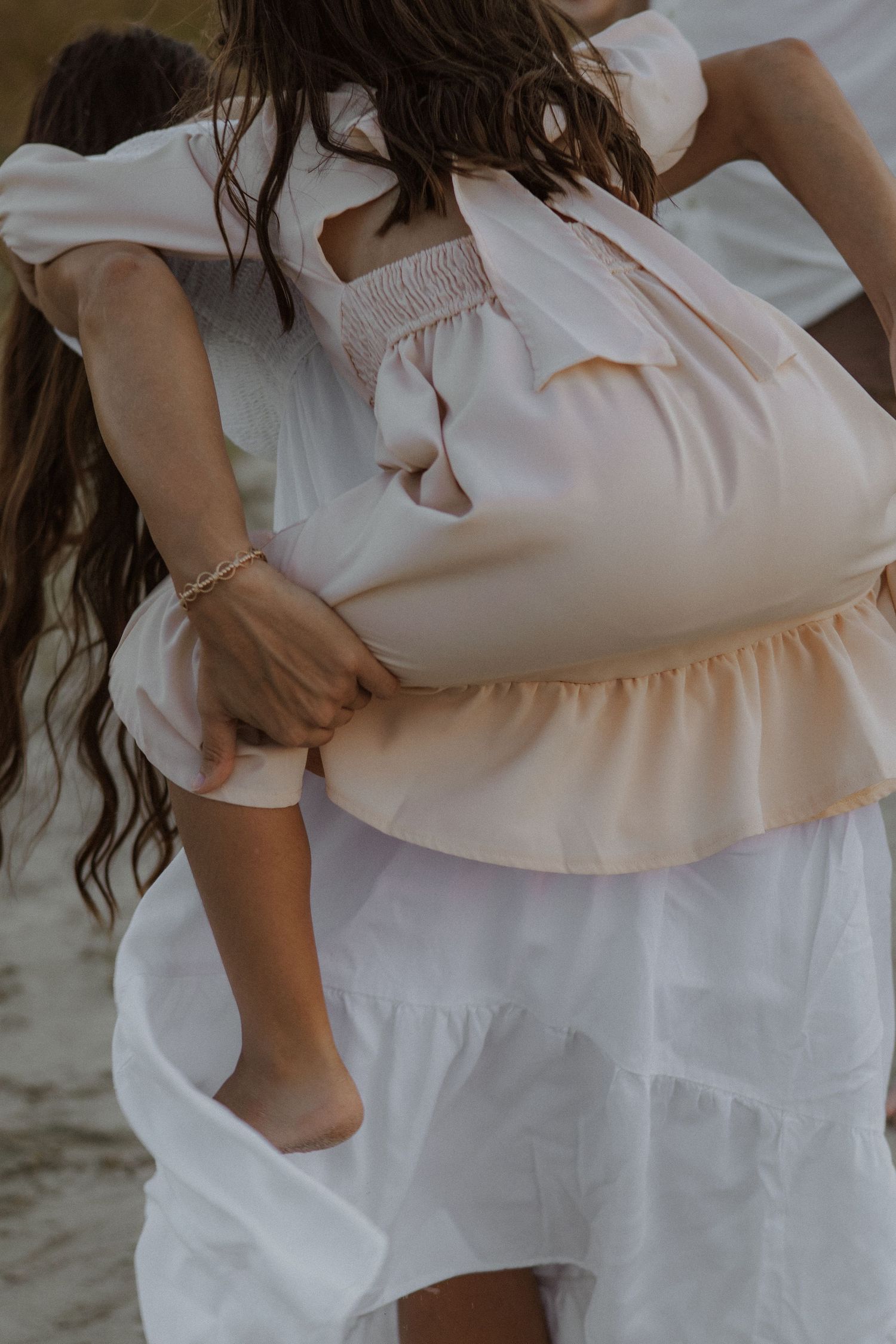 Close up detail of white and blush flowy dresses in soft beach lighting.
