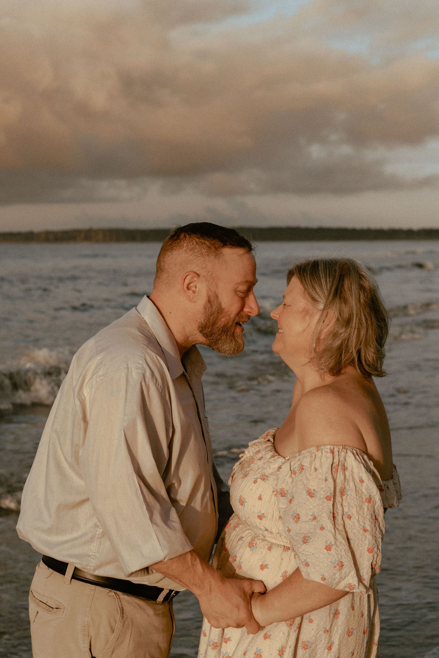 Romantic couple embracing on the beach during golden hour with waves crashing behind them.