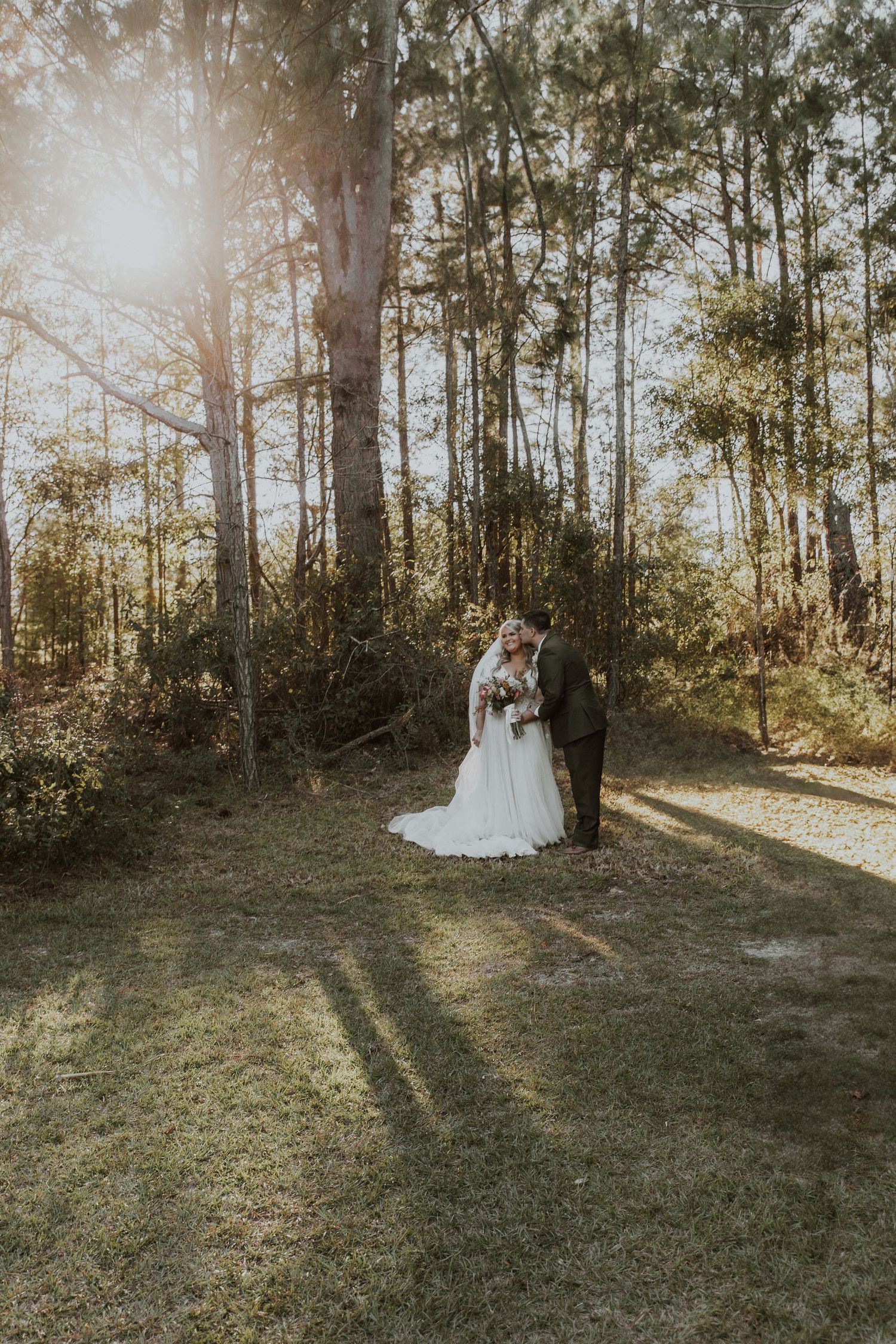 Newlyweds standing together in sunlit forest clearing during golden hour.