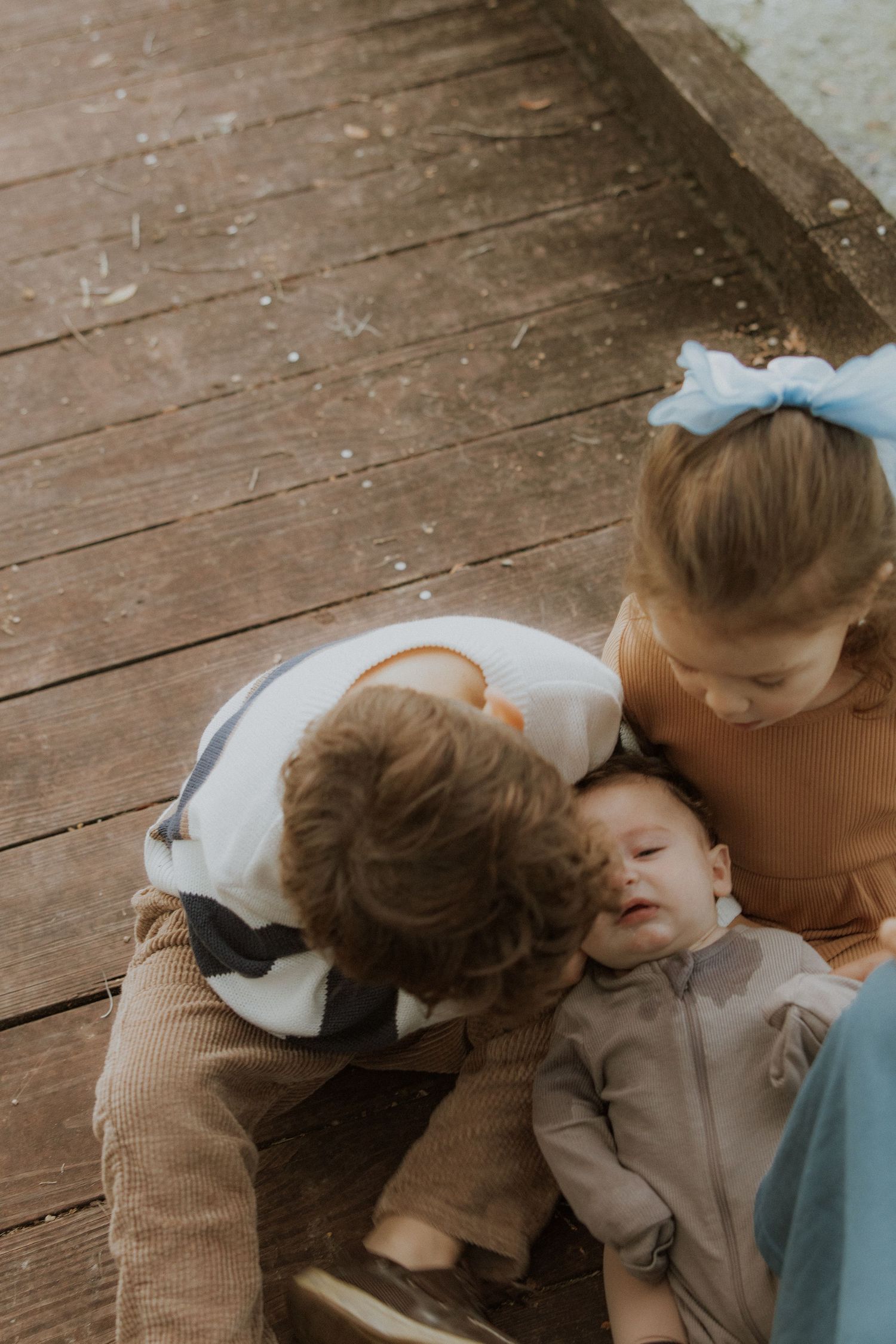 Sweet moment shared on wooden deck as children cuddle together with gentle affection.