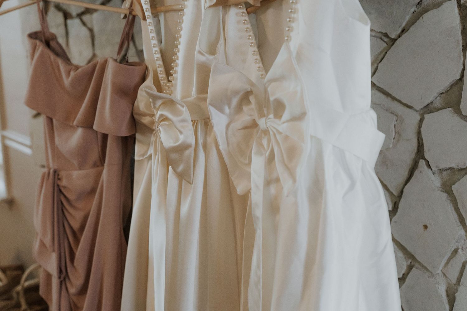 Wedding dresses in blush and ivory tones hanging on display with delicate bow details and flowing fabric.