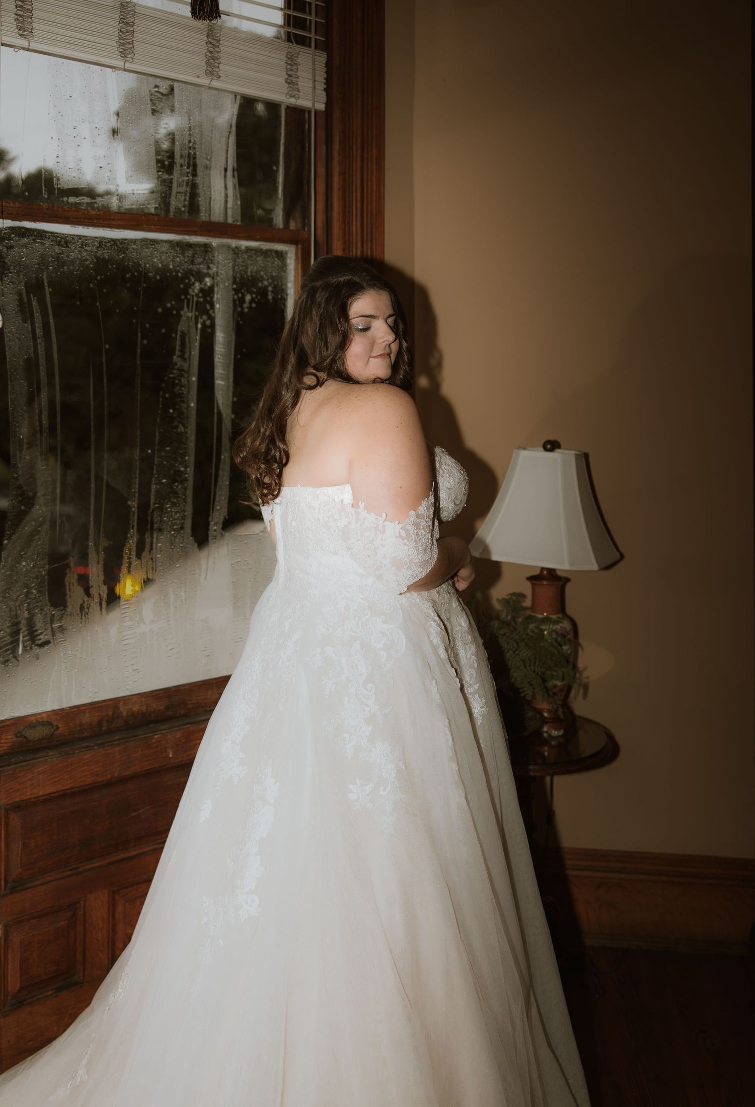 An elegant wedding dress with intricate lace details photographed indoors near a window.