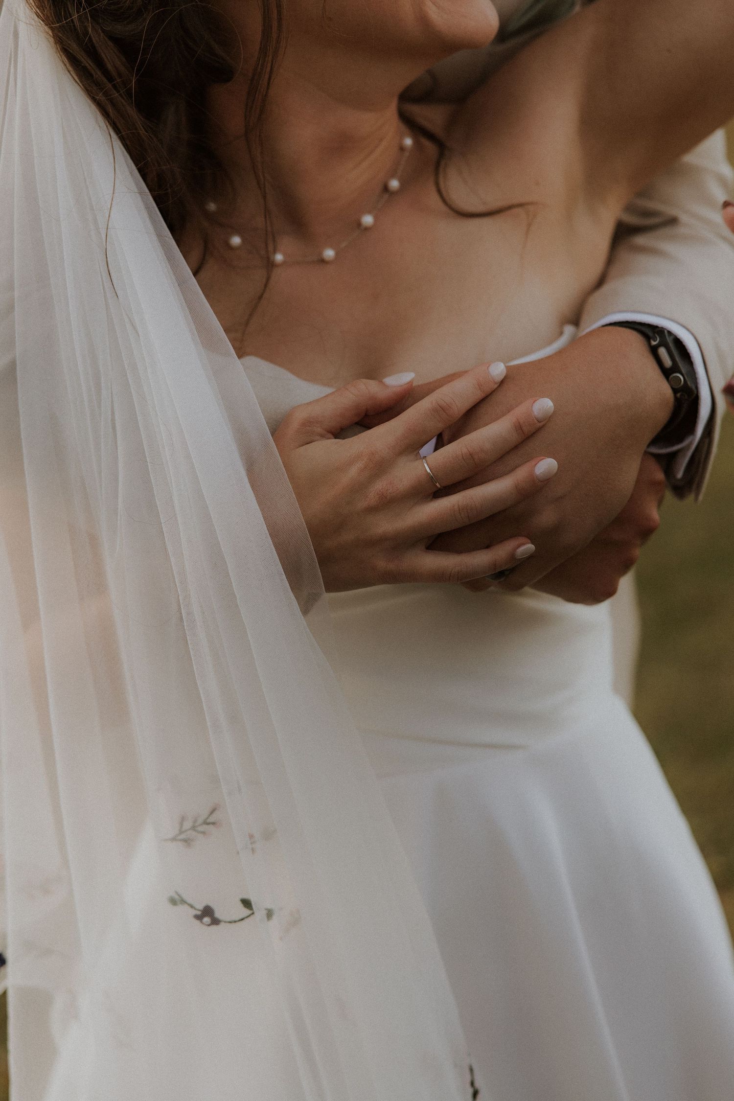 Close-up detail of a bride's hand with engagement ring touching a groom's arm during a wedding ceremony.