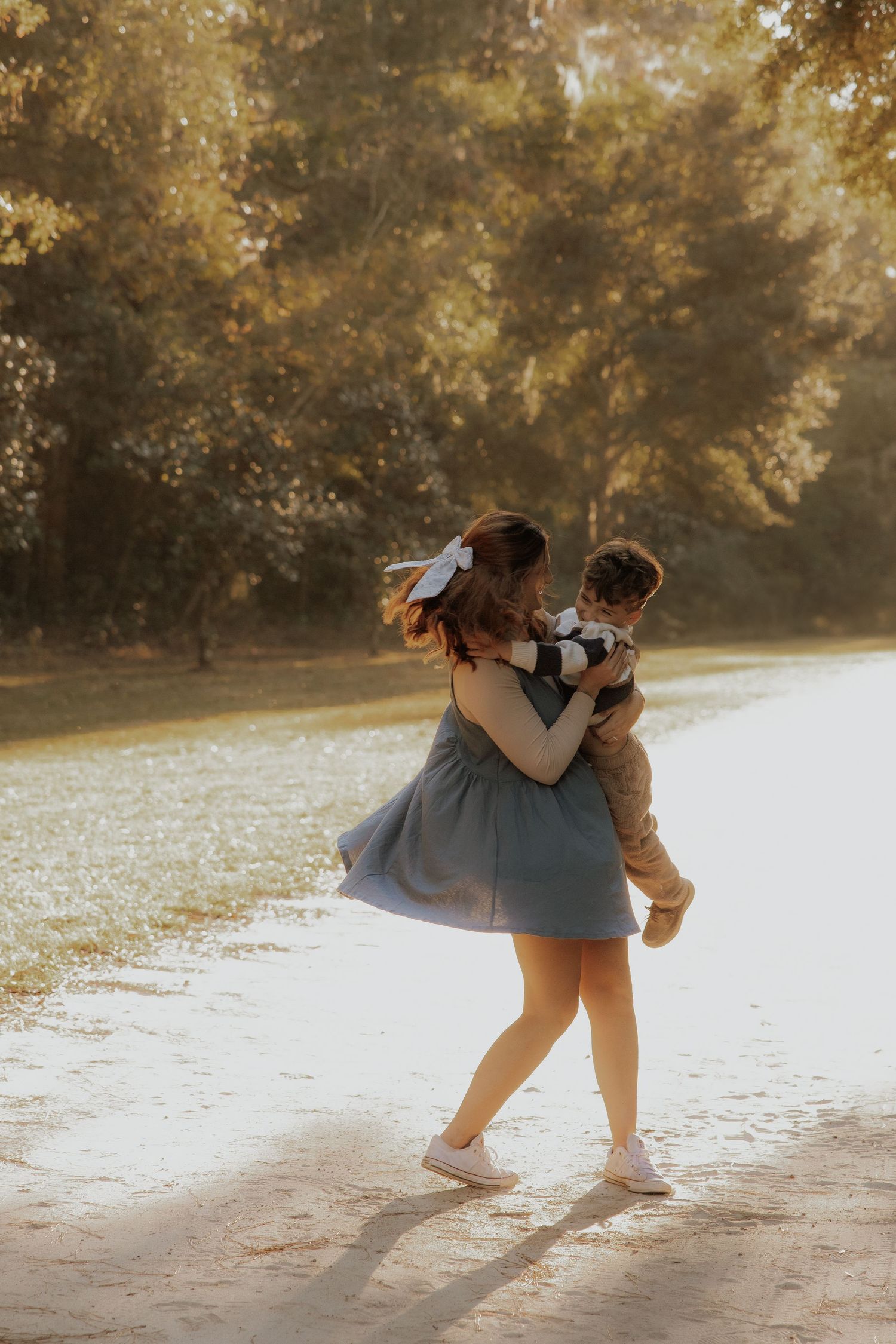 A tender embrace captured in golden sunlight as a couple spins joyfully on a path surrounded by autumn trees.