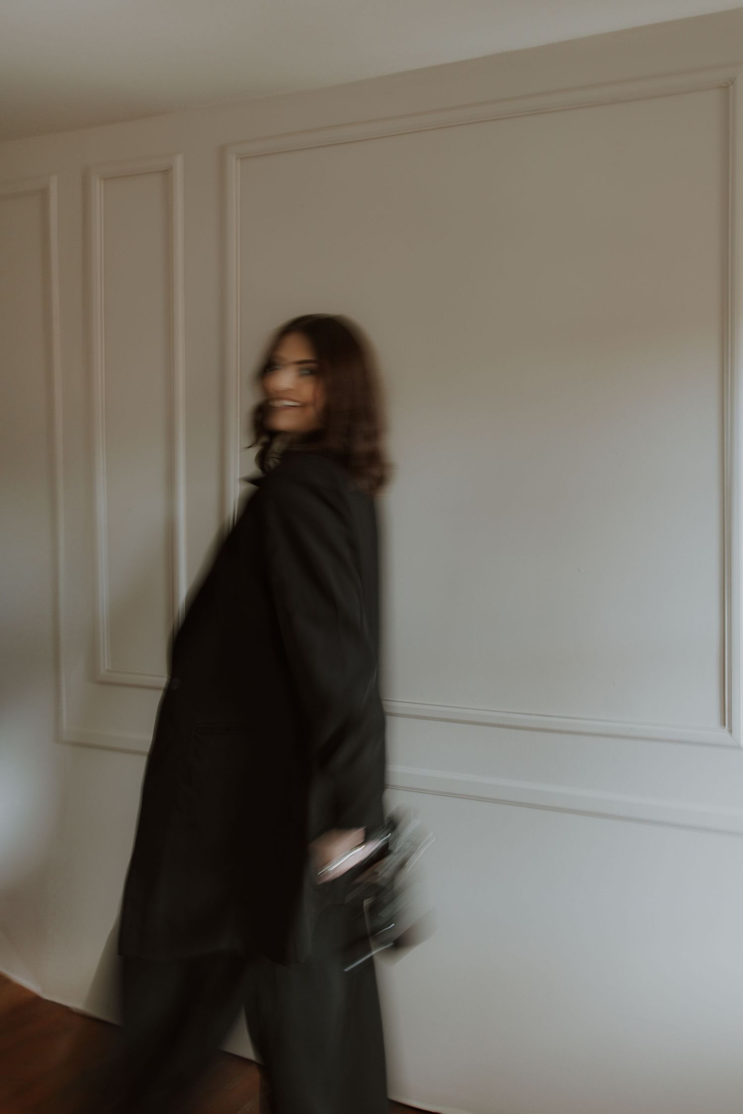 Person in black outfit poses dramatically against white paneled wall.
