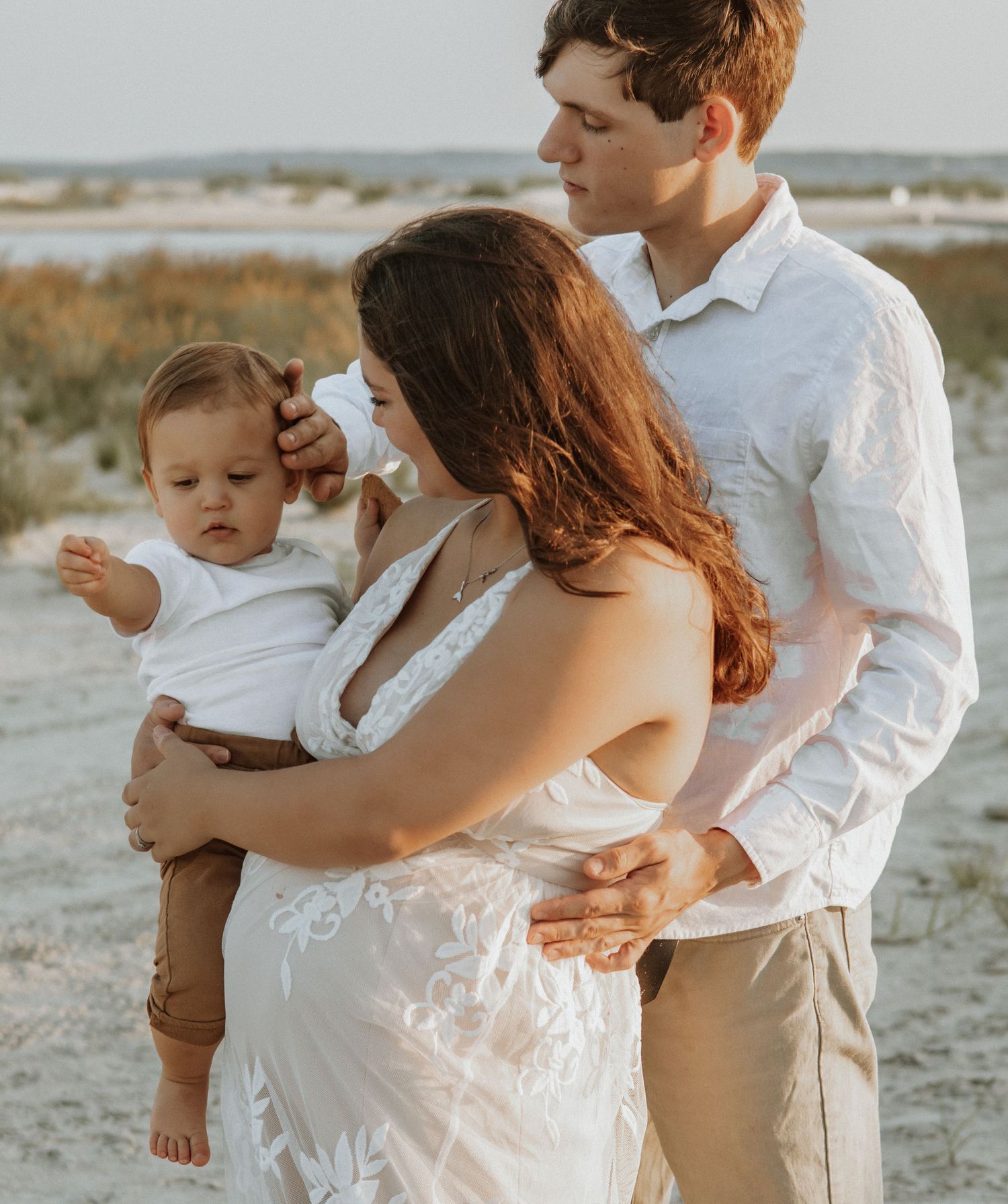 Family embracing on beach at sunset wearing white dress and light colored clothing.