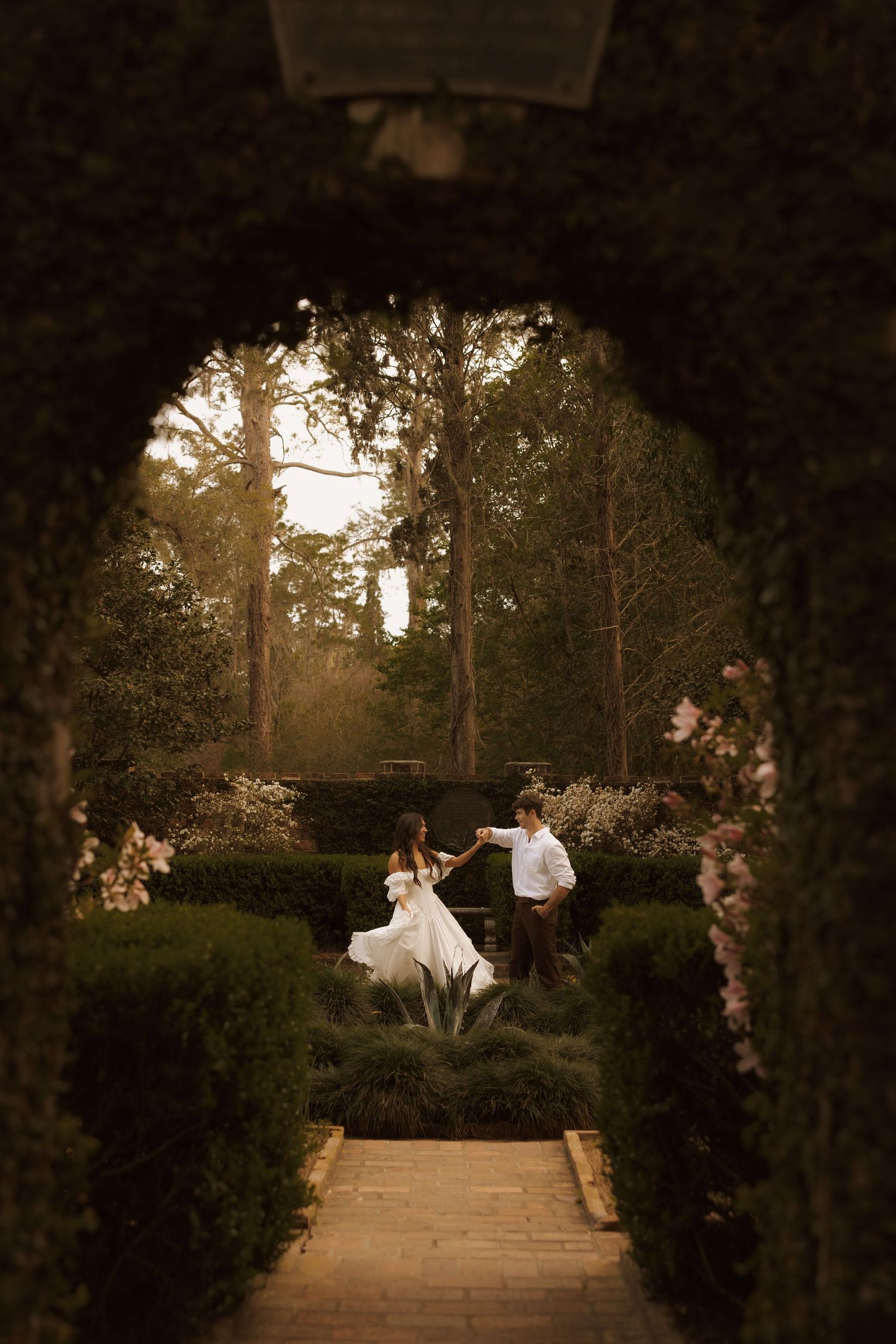 Couple dancing in a lush garden archway at golden hour, bride in white gown, romantic outdoor wedding photography.