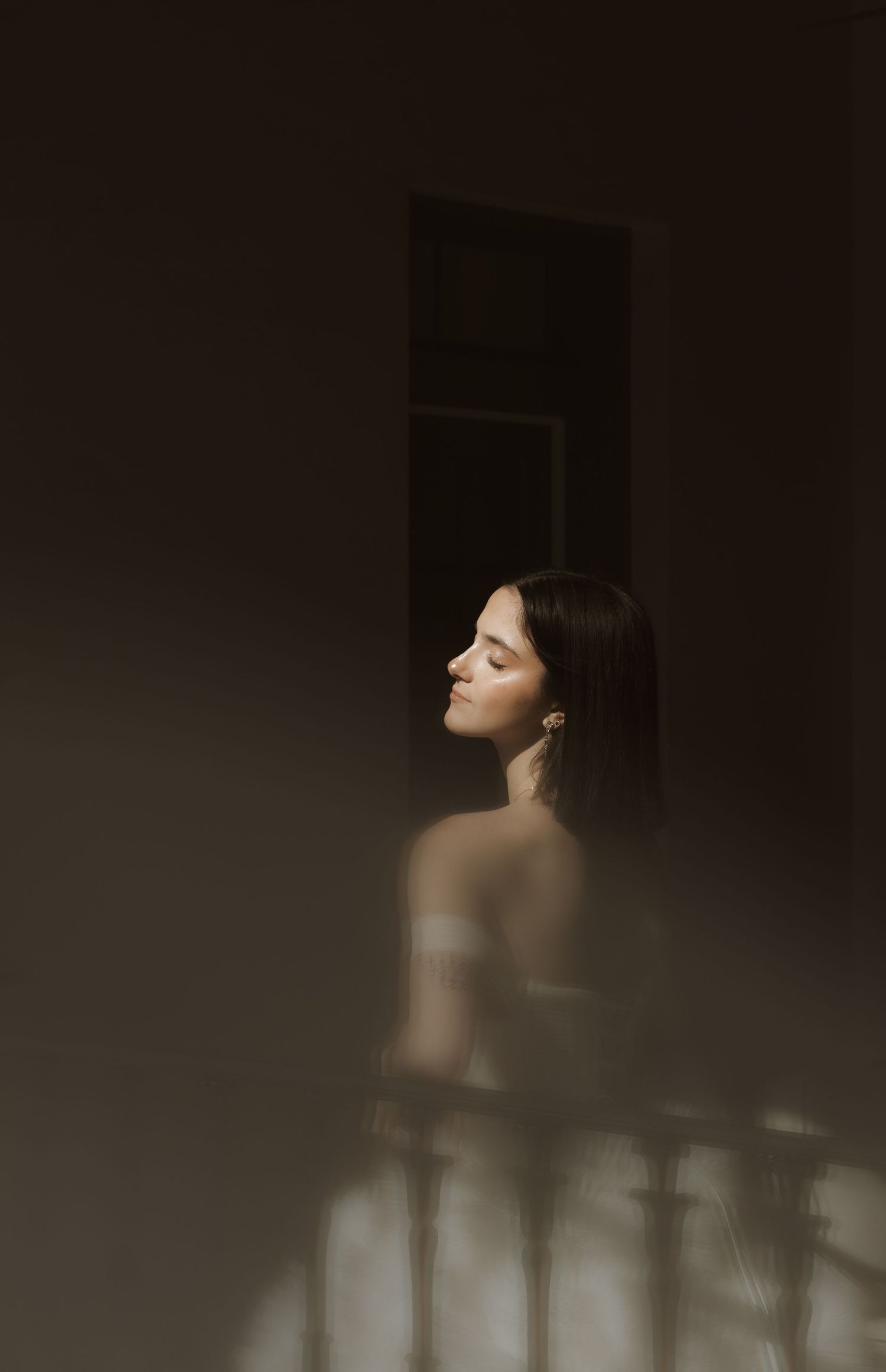 Artistic portrait in moody lighting shows a silhouette against dark background with dramatic shadows and contrast.