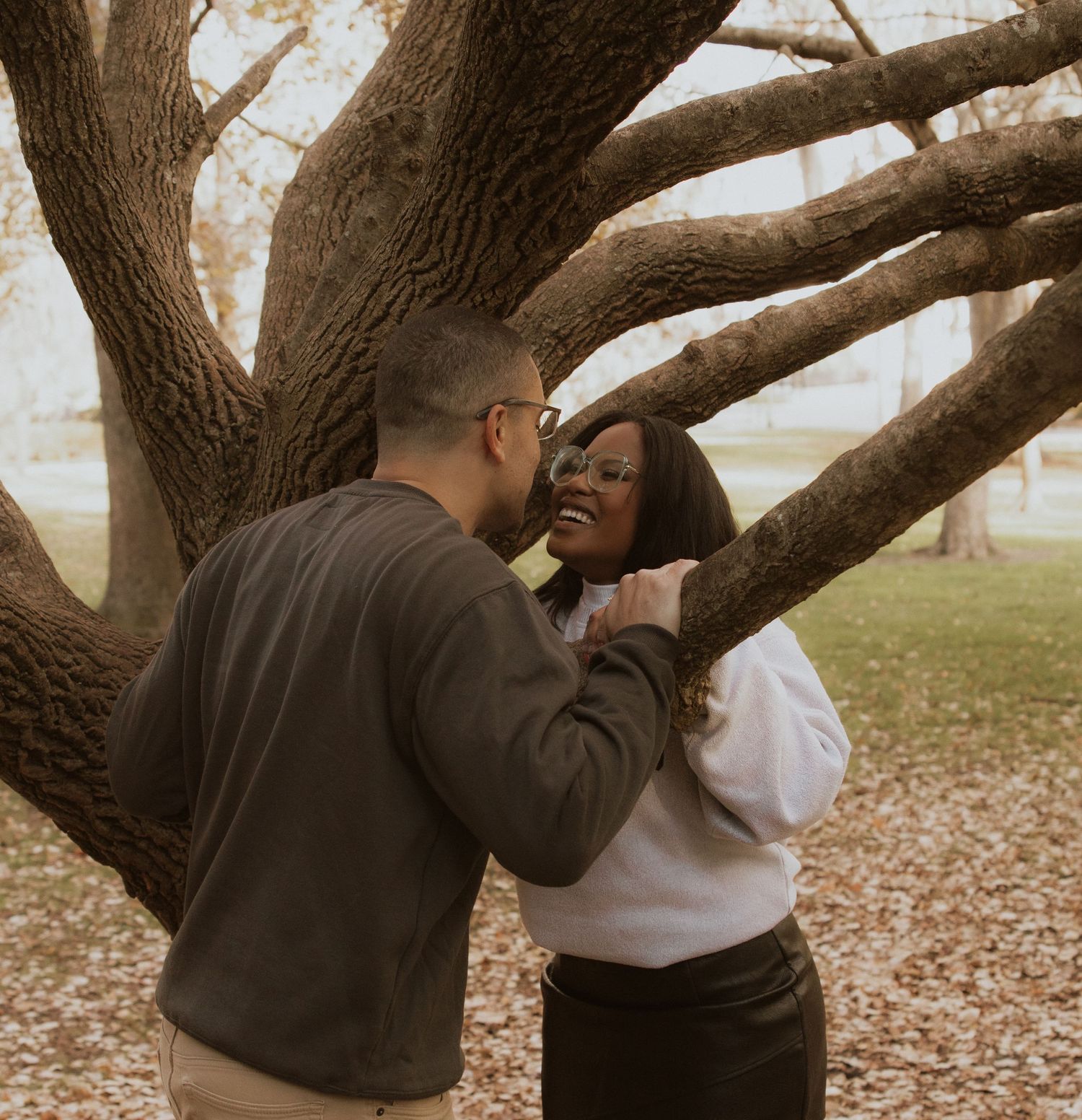Intimate moment shared between couple beneath sprawling tree branches.