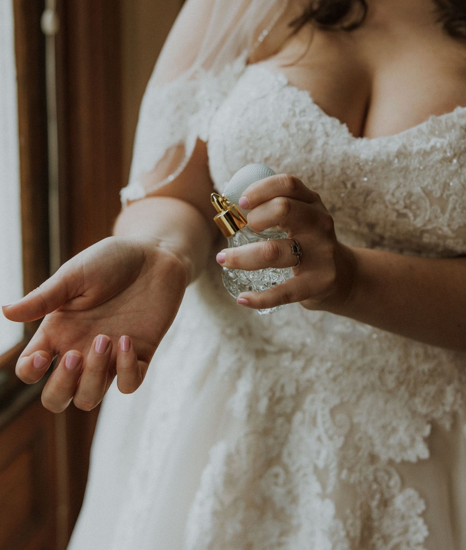 Bride spraying perfume on her wrist in a delicate lace wedding dress.