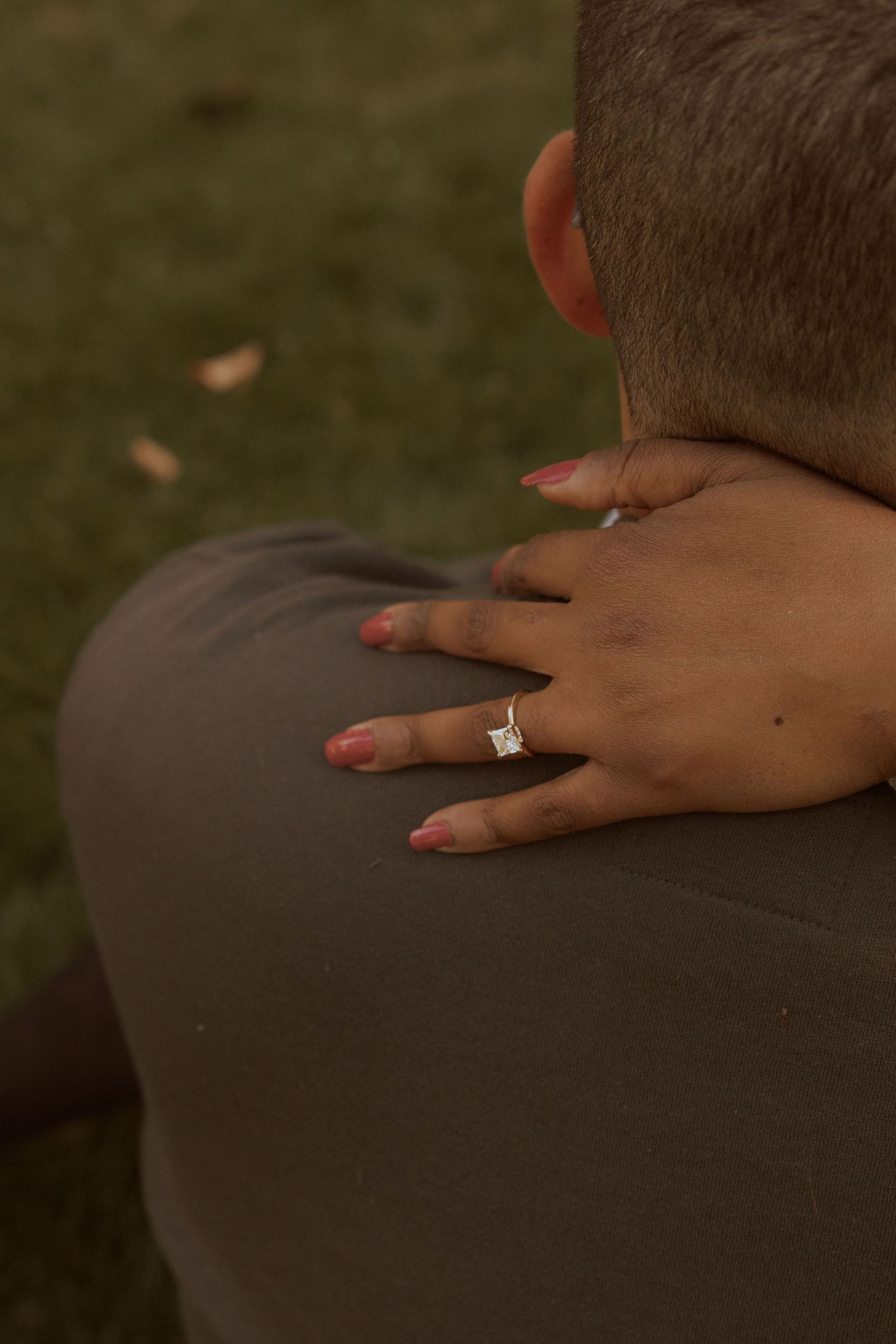 Close-up shot of hands with engagement ring resting on shoulder during intimate moment.