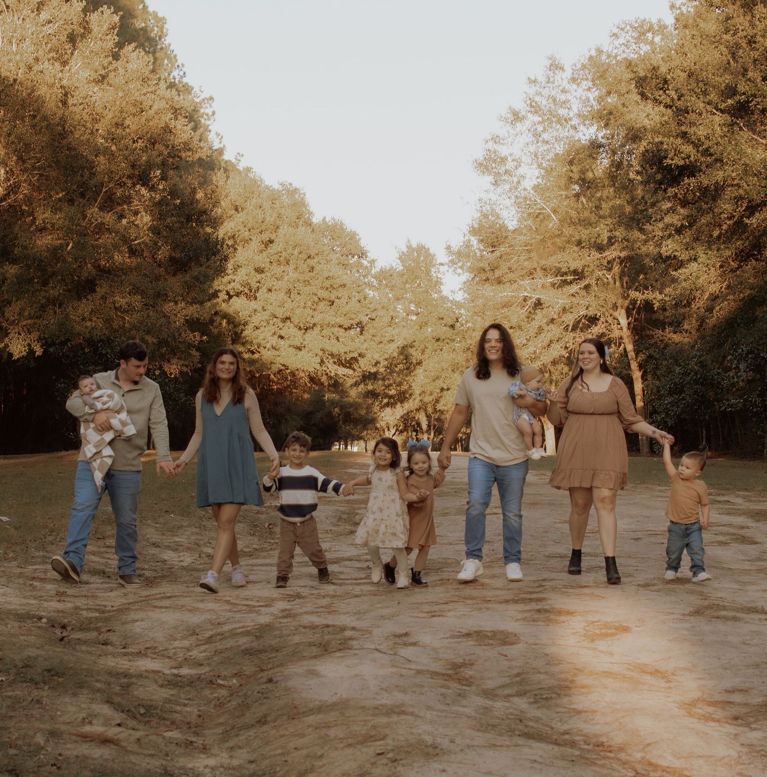 A group of people hold hands in a line while enjoying an autumn day in the woods.