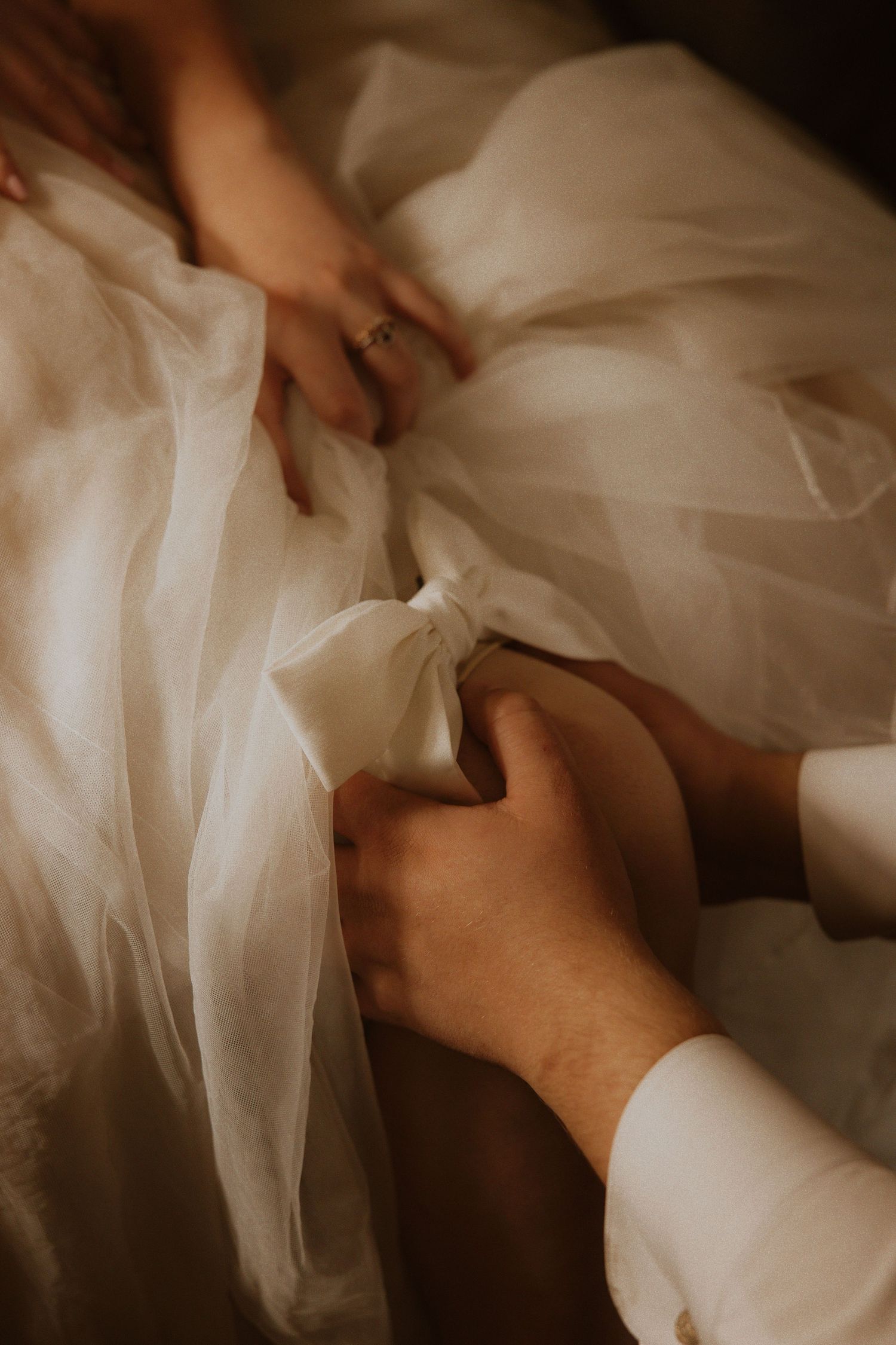 Close-up of hands adjusting layers of white tulle fabric on a wedding dress.