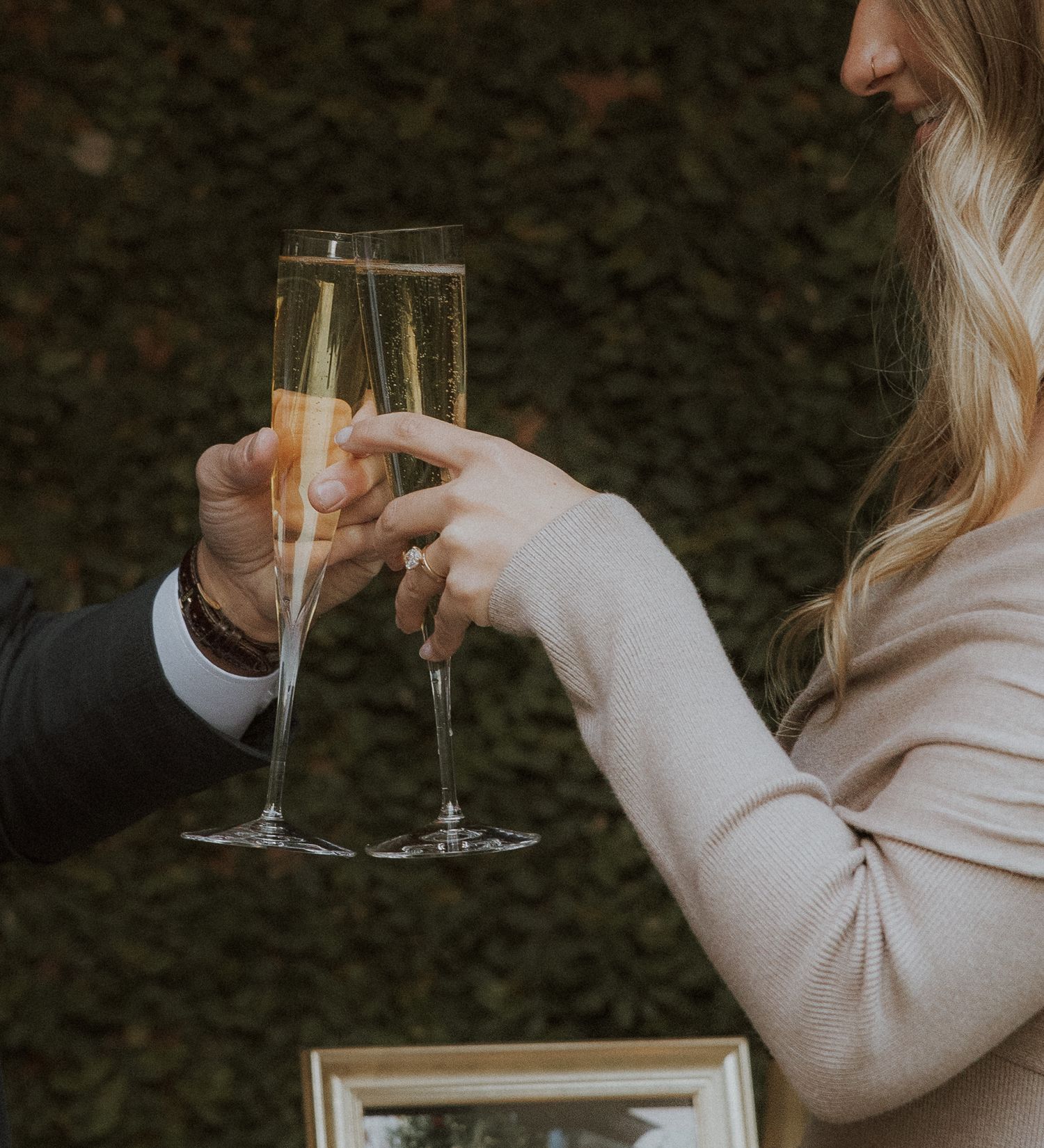 Hands toasting with champagne flutes against dark background.
