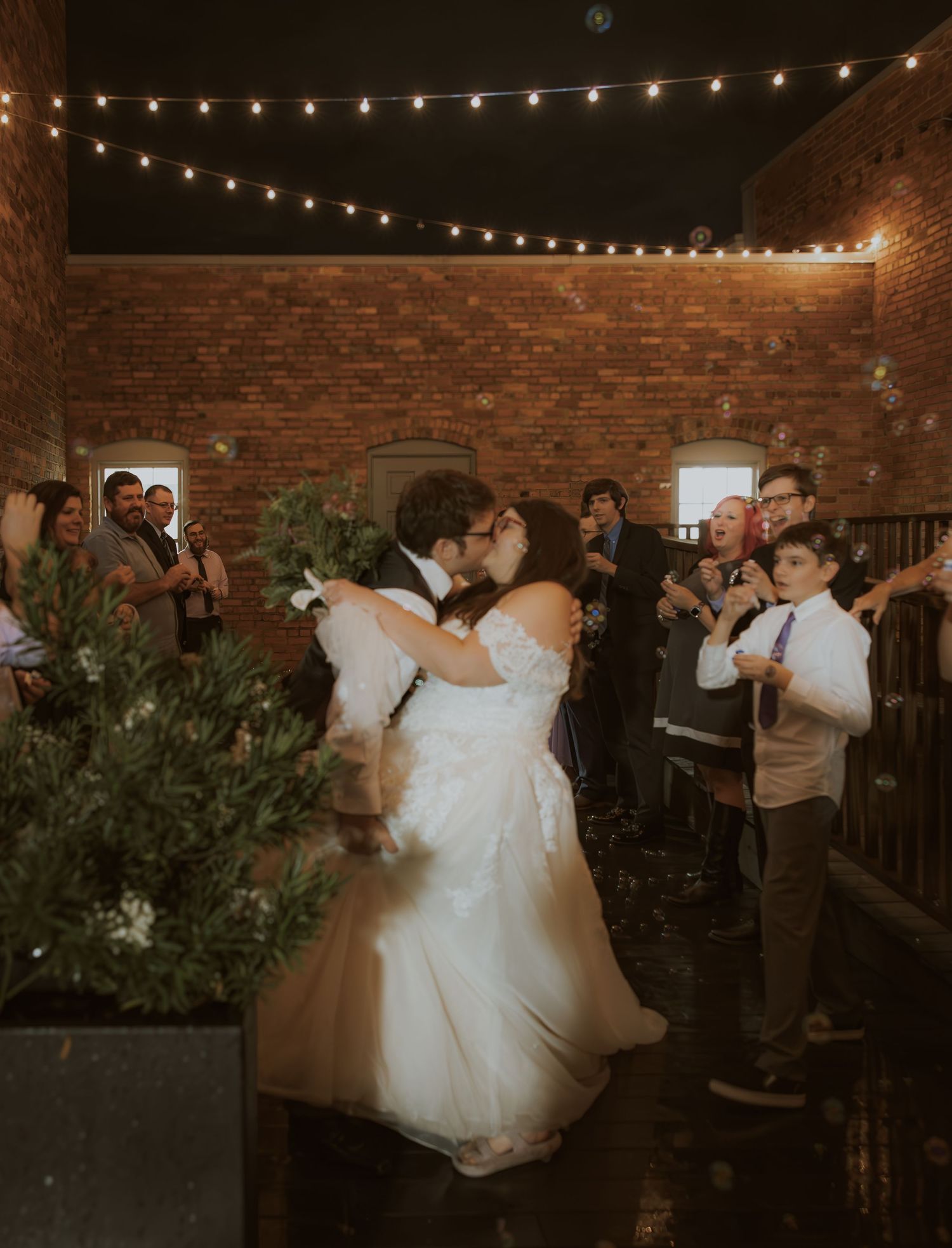 First dance at wedding reception under string lights in rustic brick venue.