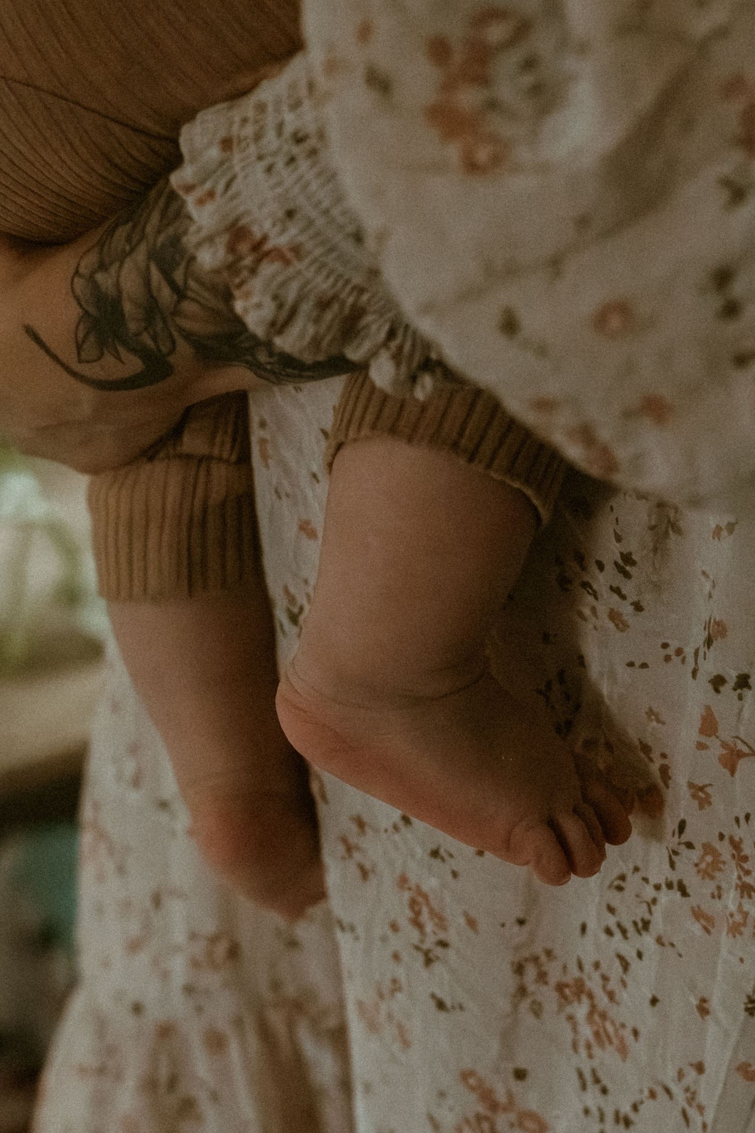 Close-up of baby's bare feet against floral fabric in soft lighting.