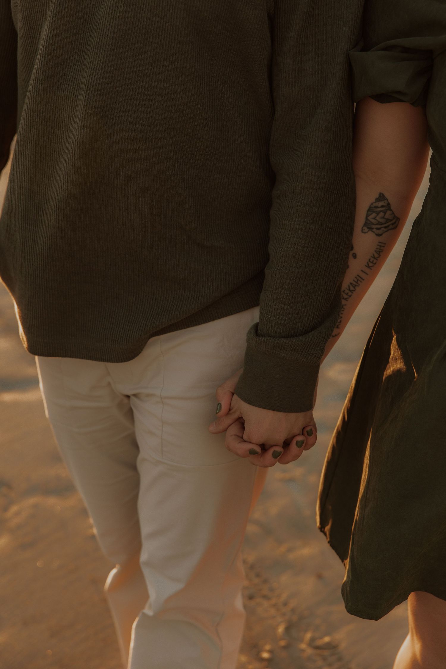 Couple holding hands while wearing coordinated green and white outfits with visible tattoo.