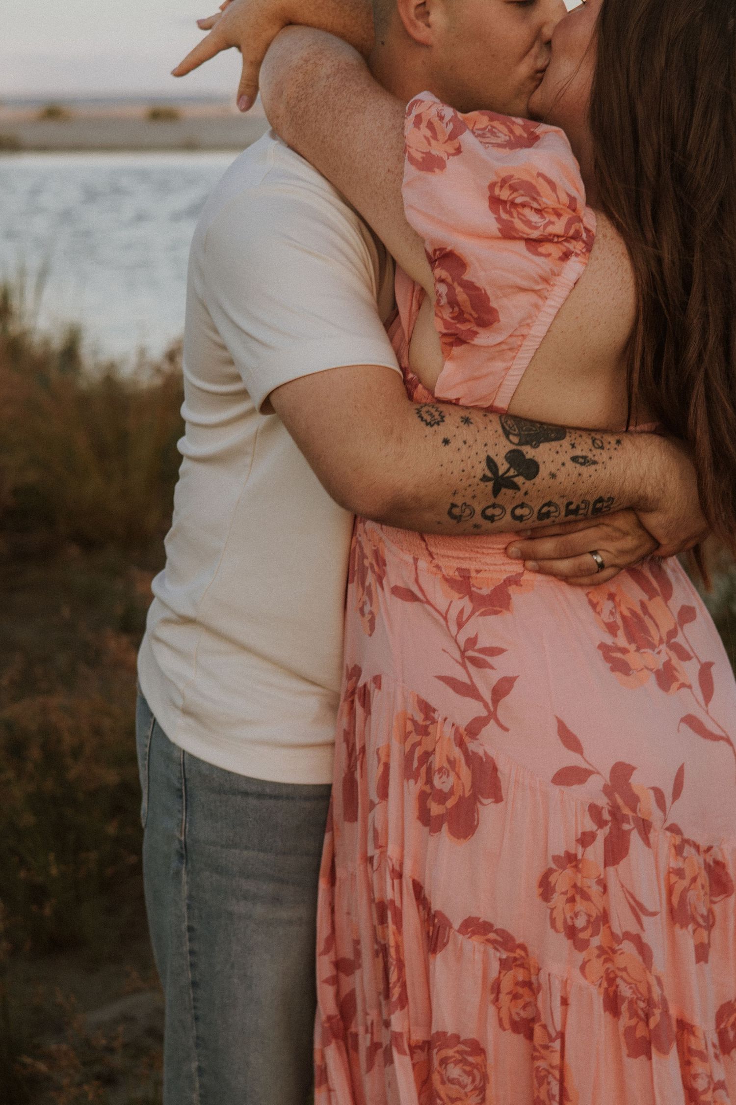 Close up of couple embracing, showing floral dress detail and tattoo on arm.
