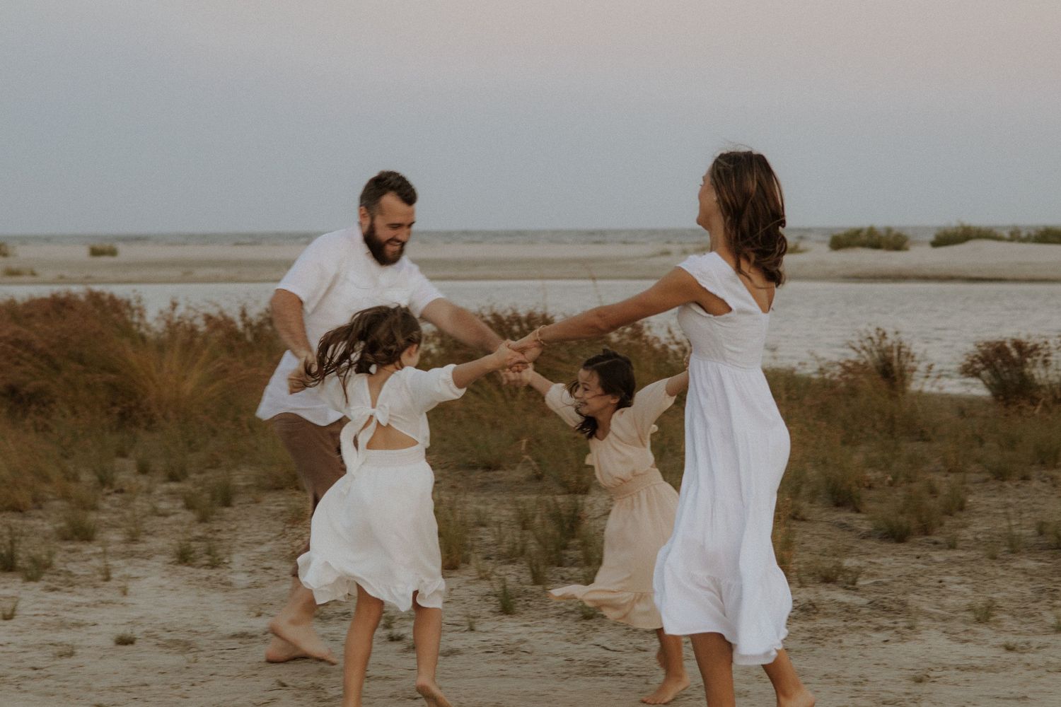 A family in white outfits dances together on a beach at sunset.