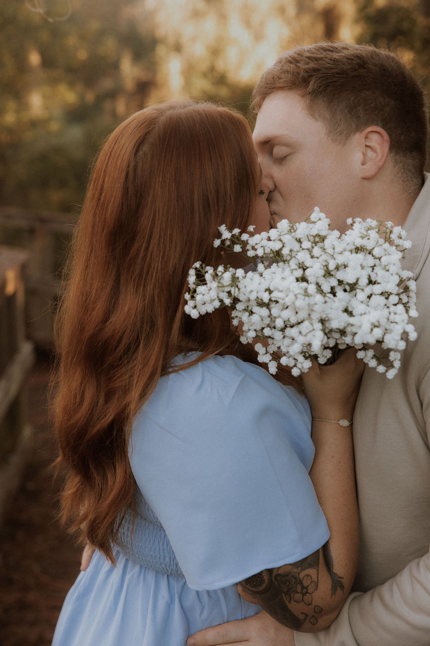 Romantic kiss with baby's breath flowers held between couple in soft lighting.