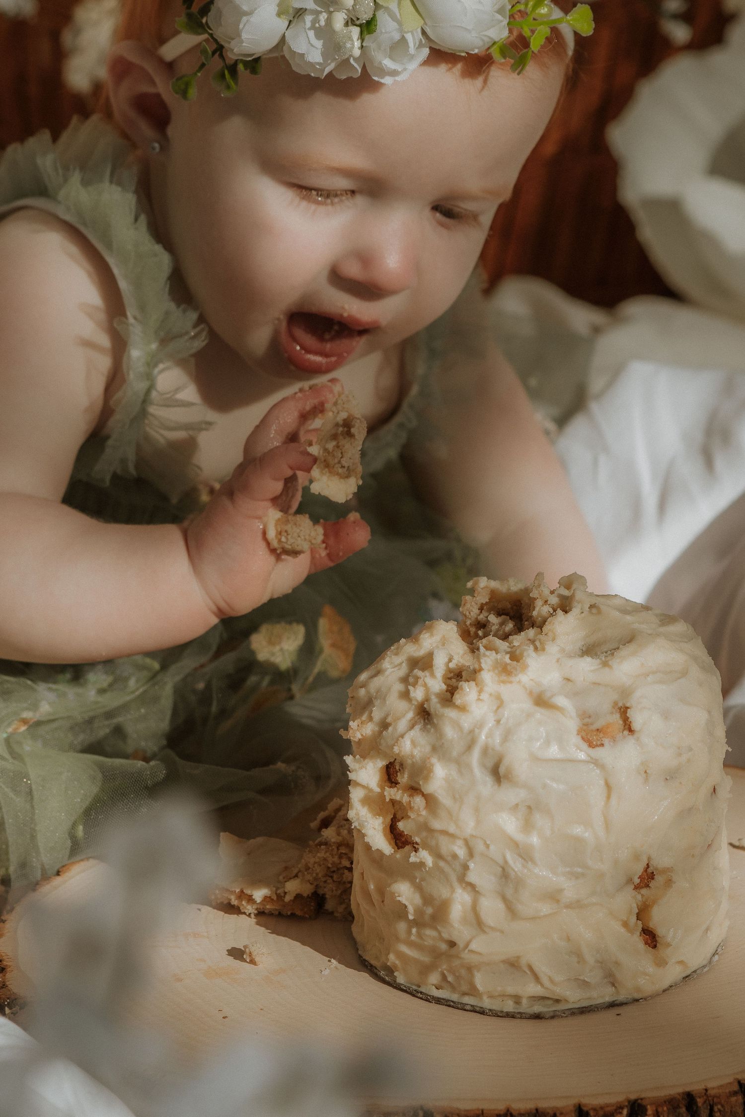 Baby in green dress enjoying small white frosted cake.