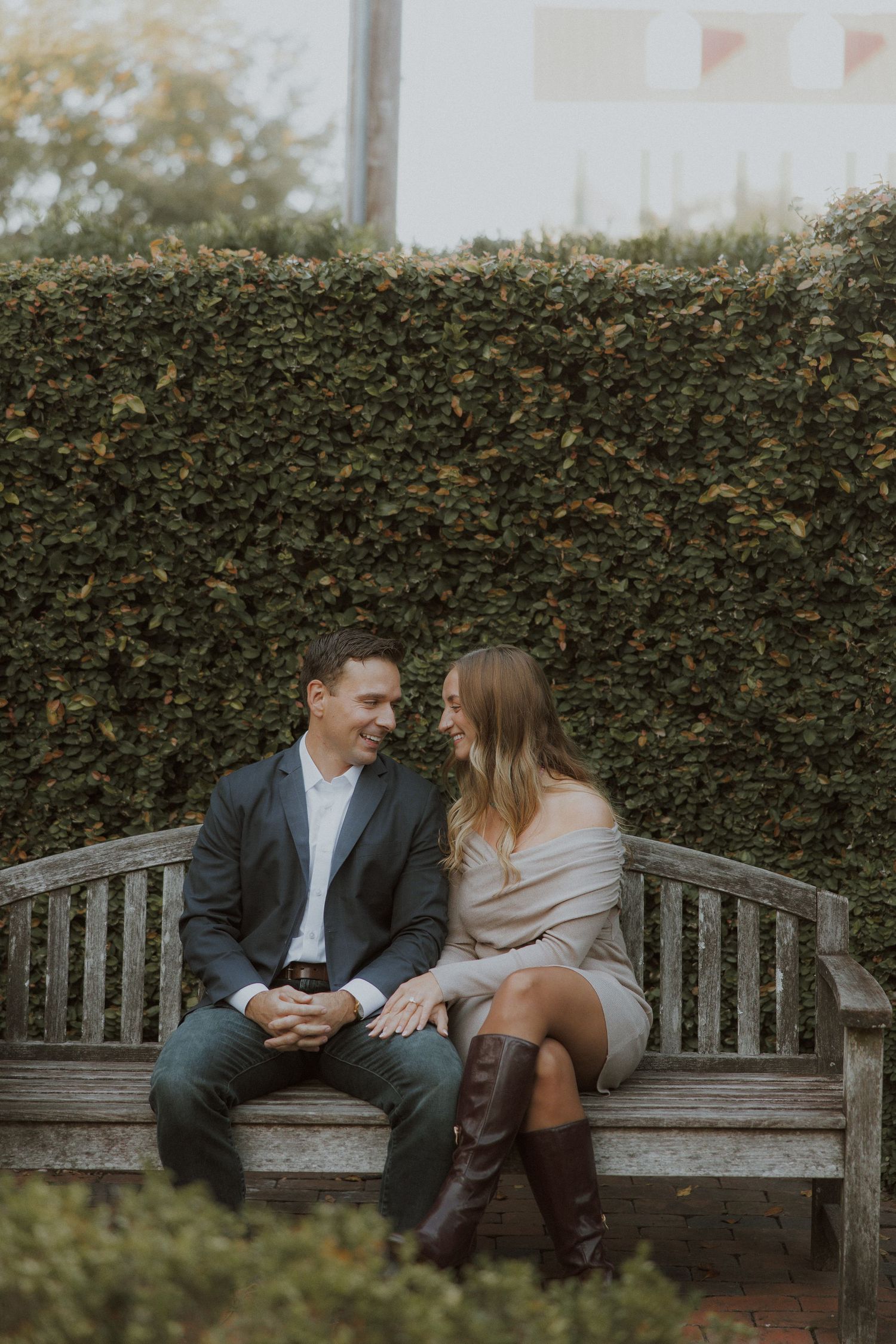 Couple sitting together on wooden bench in front of ivy-covered wall.