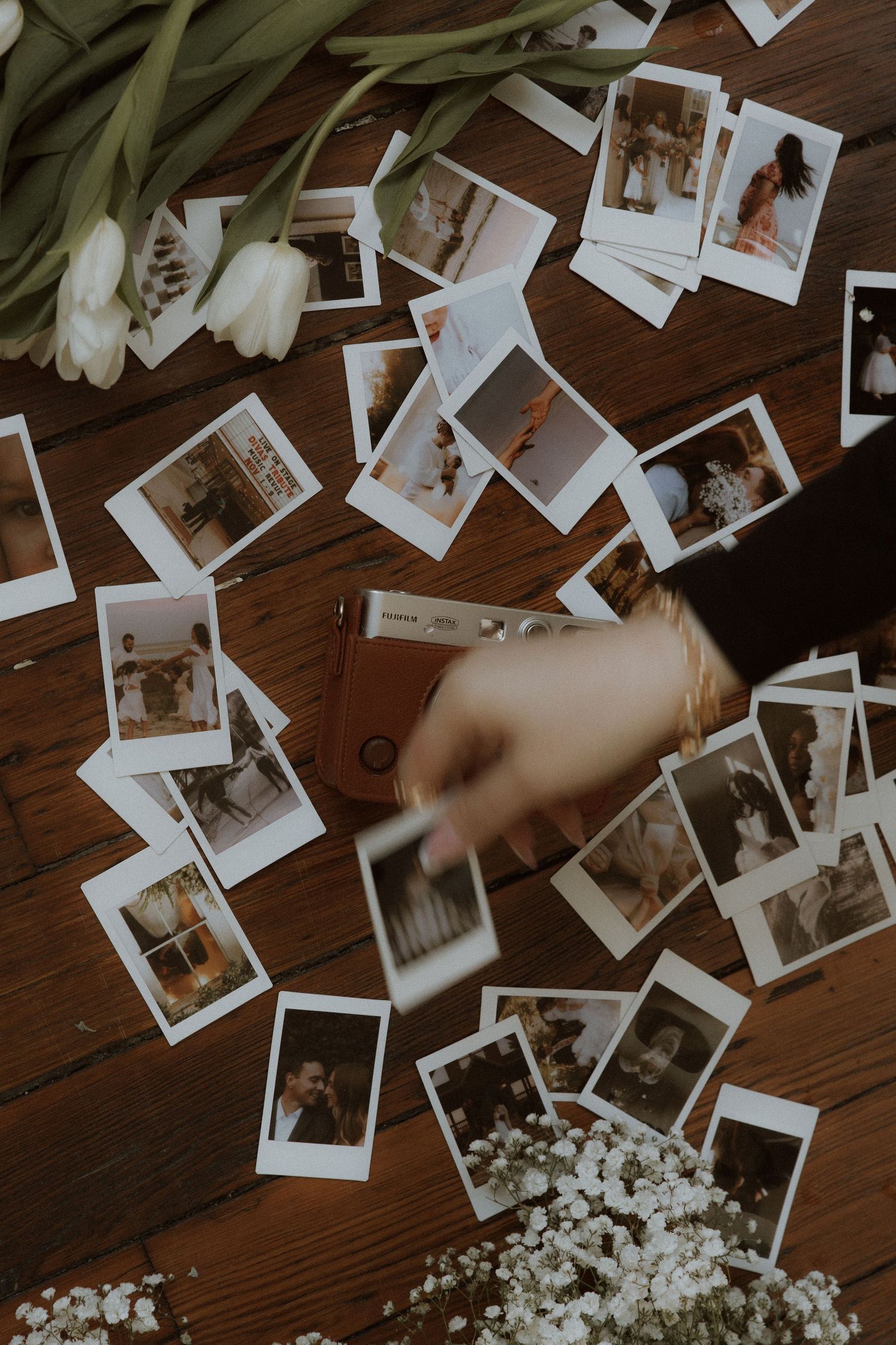 Polaroid photos scattered on wooden table with white tulips and flowers.