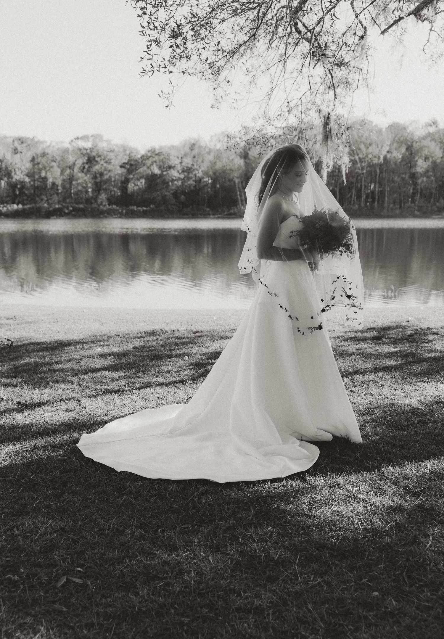 Elegant wedding portrait by a serene lake in black and white photography.
