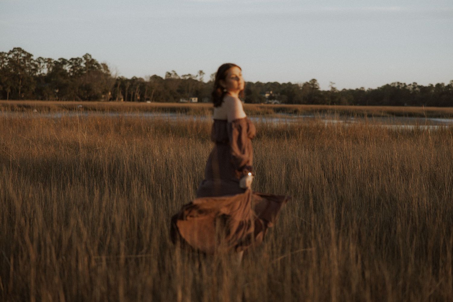 Person in dress poses in golden grass field at sunset.