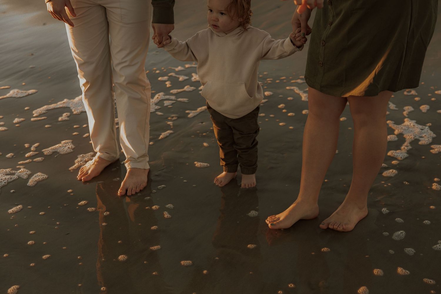 Barefoot family members walking together on a sandy beach at sunset.