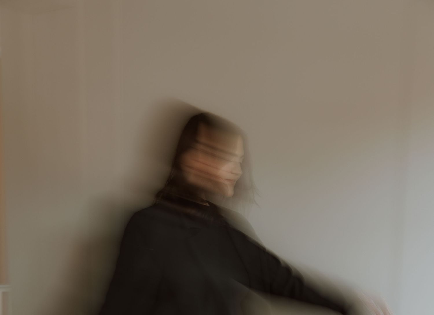 Motion-blurred portrait showing movement against beige wall.