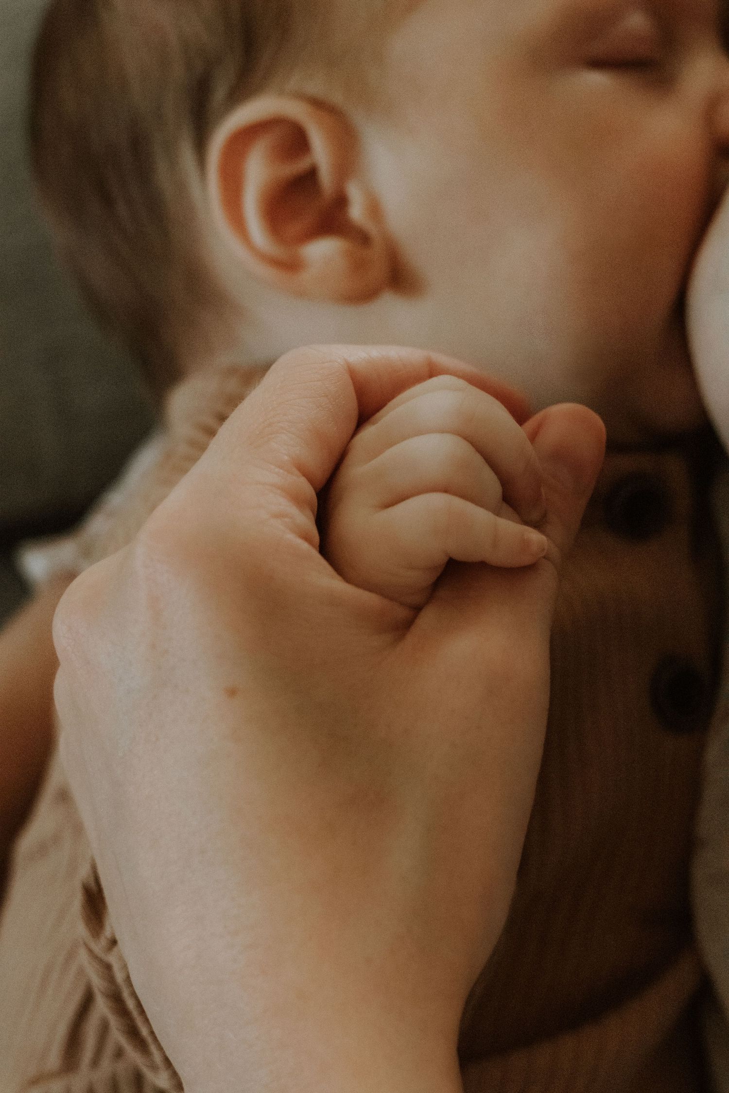 Close-up of baby's tiny hand grasping parent's finger in warm lighting.