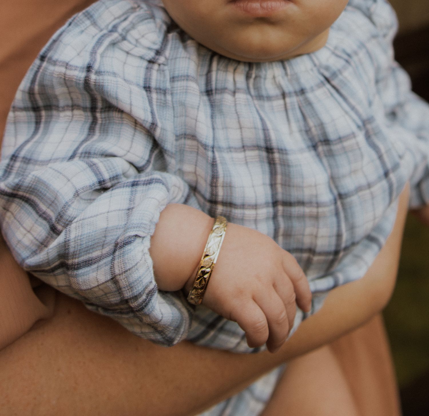 Close up of a baby wearing a plaid outfit with a delicate gold bracelet.