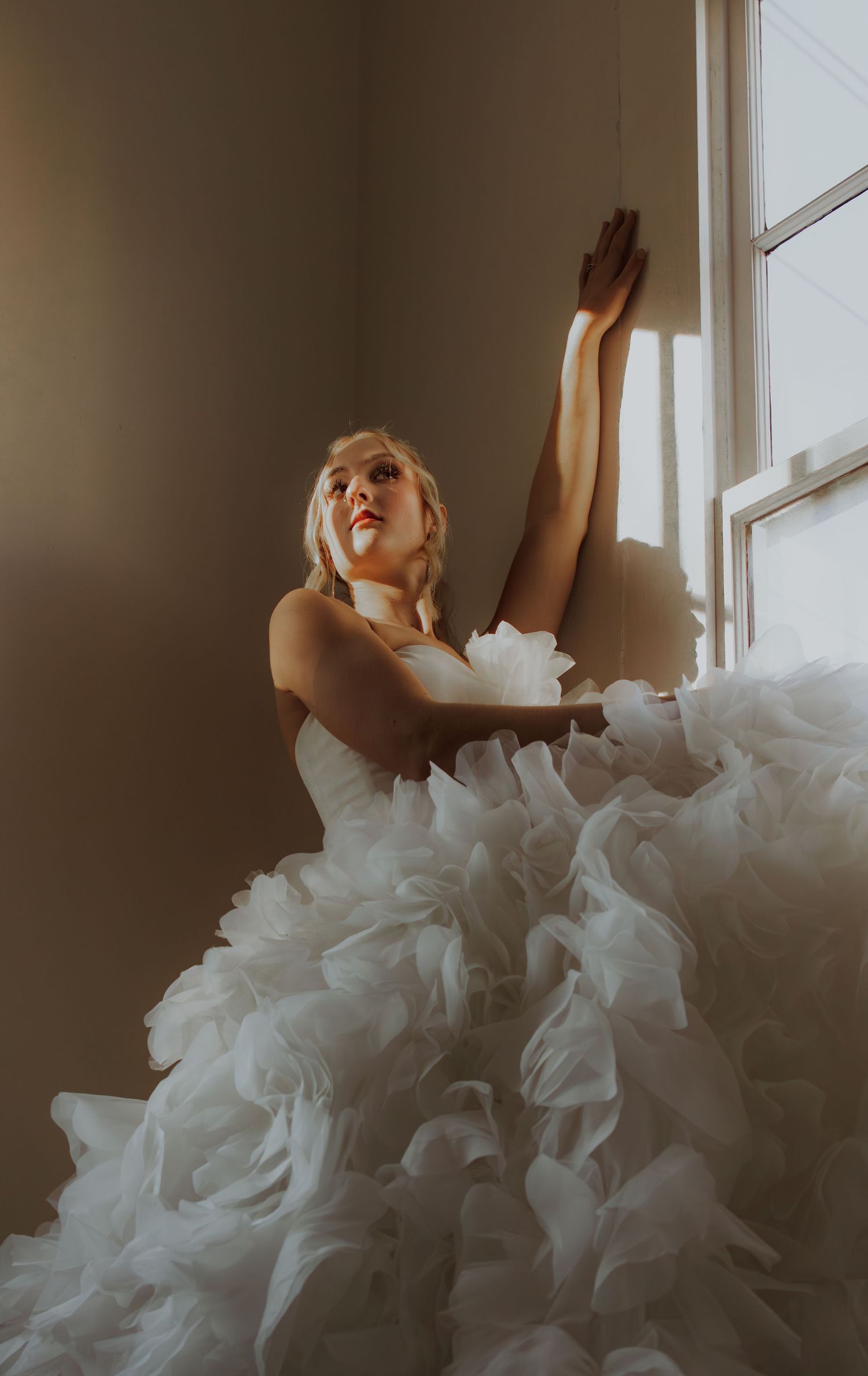 Person in flowing white wedding dress reaching toward window light.