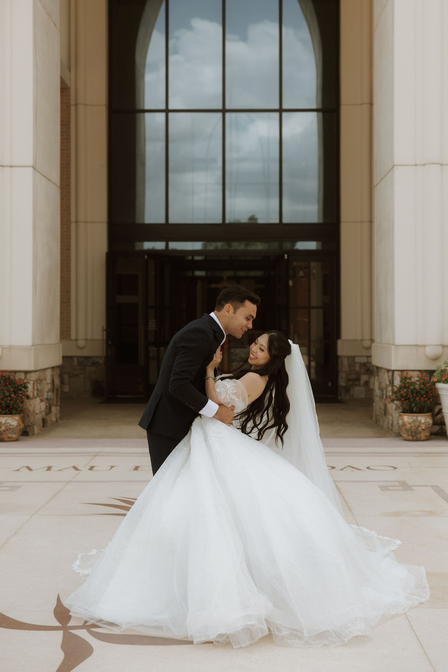 Newlywed couple in formal wedding attire dancing gracefully across the patio of a grand columned building.