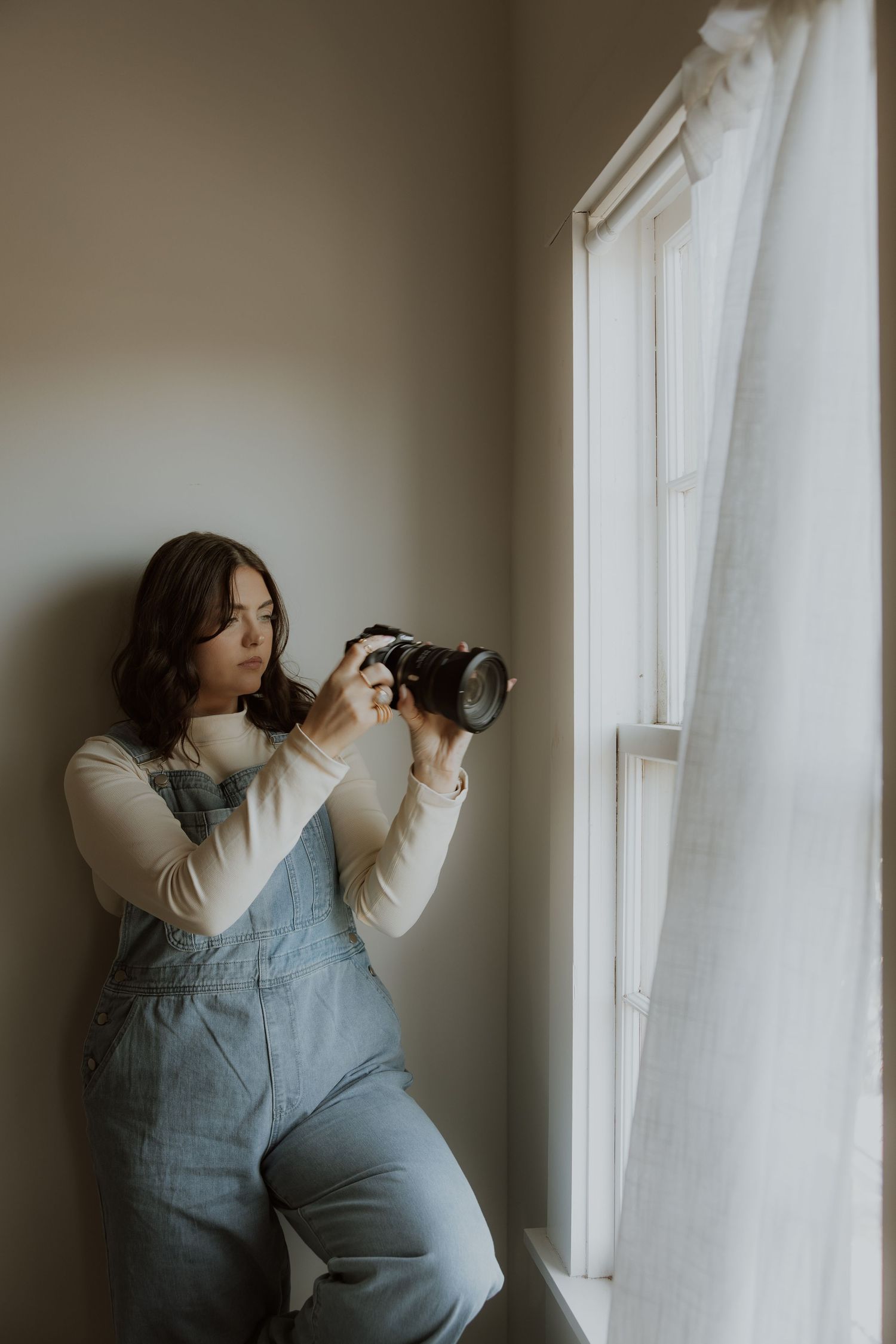 Photographer in overalls takes pictures by window in natural light.