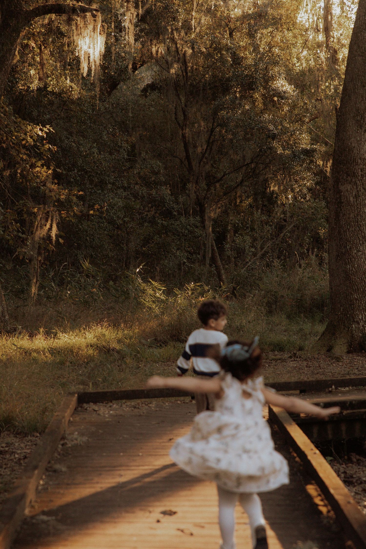 Children run along a wooden boardwalk path through a mossy forest.