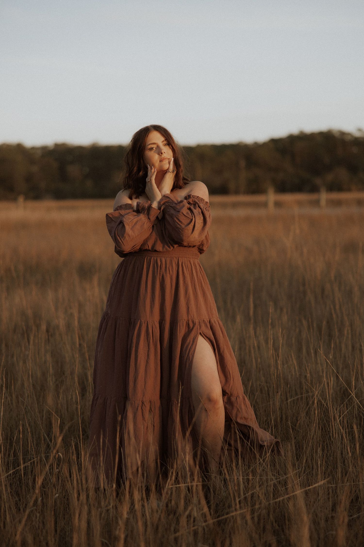 A brown maxi dress with a slit flows in a golden field during sunset.