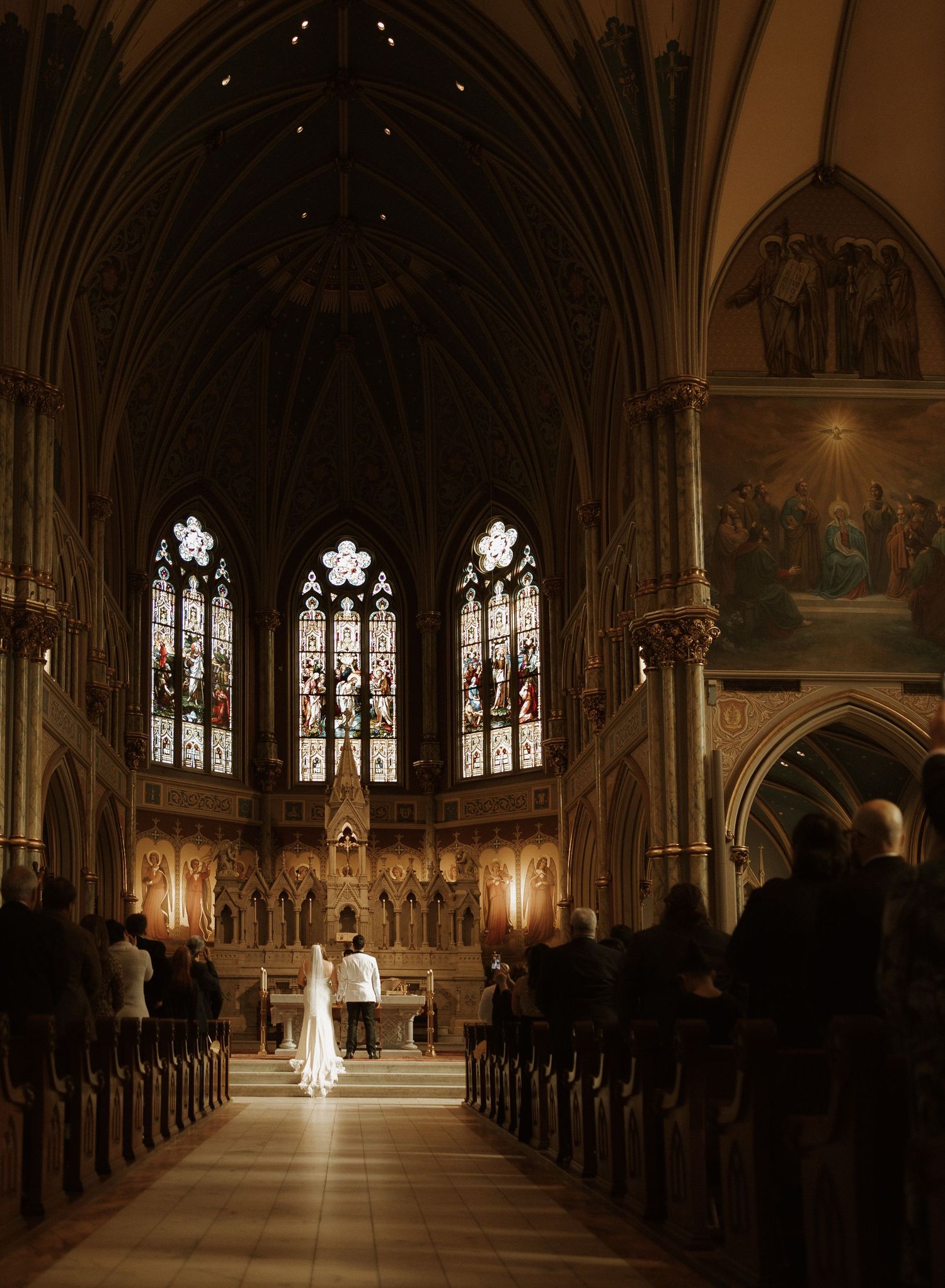 A traditional church wedding ceremony in a Gothic cathedral with stained glass windows and vaulted ceilings illuminated in warm light.