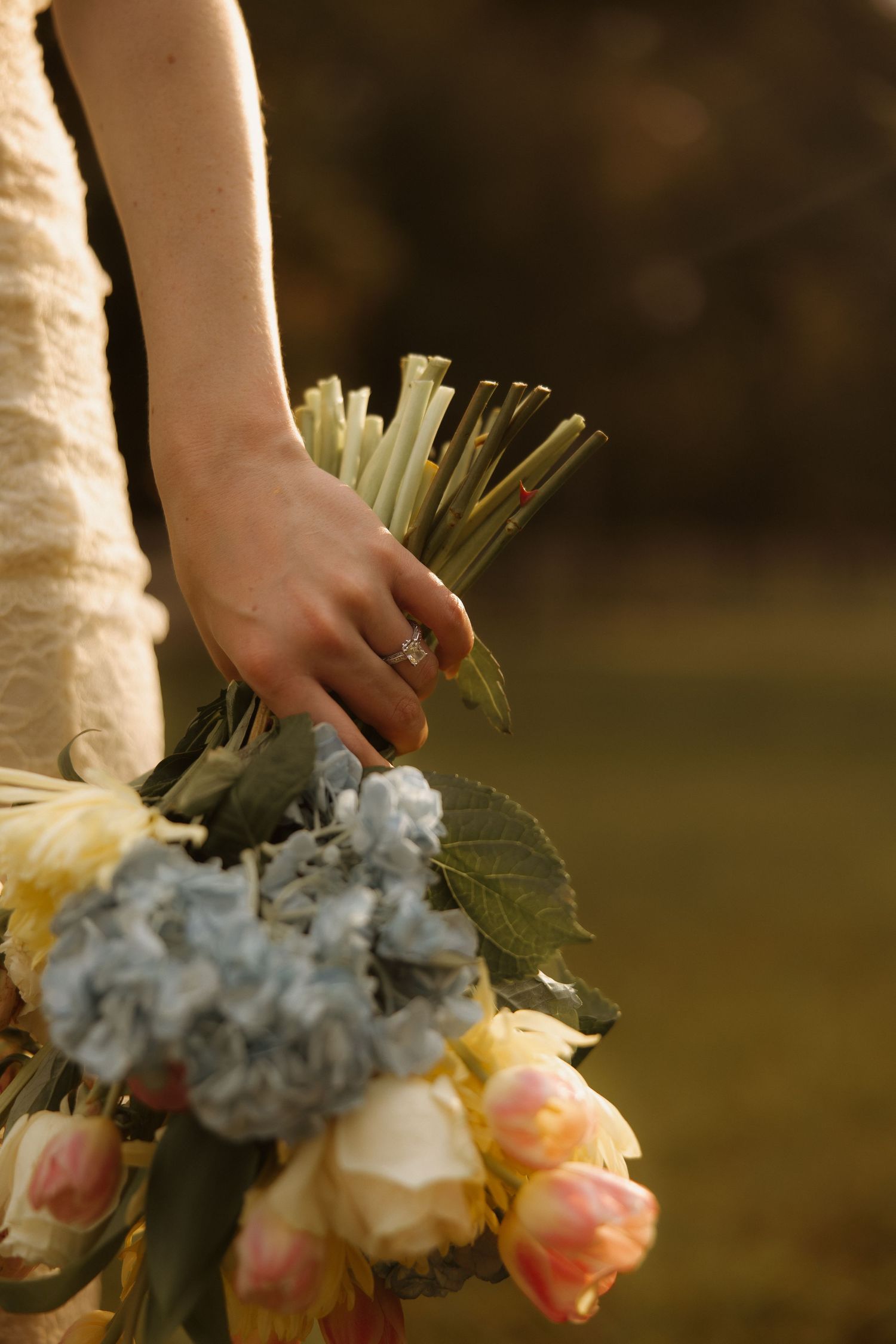 Bride holding a wedding bouquet of blue hydrangeas, pink tulips, and white roses, wearing a diamond engagement ring.
