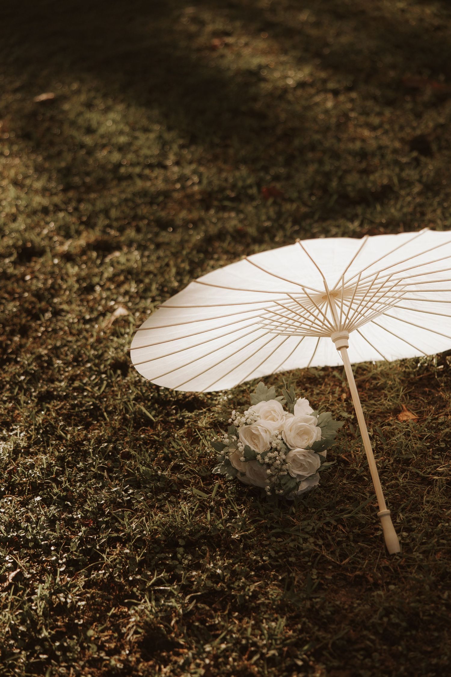 White paper parasol laying on dark ground with delicate floral details visible in sepia-toned artistic composition.
