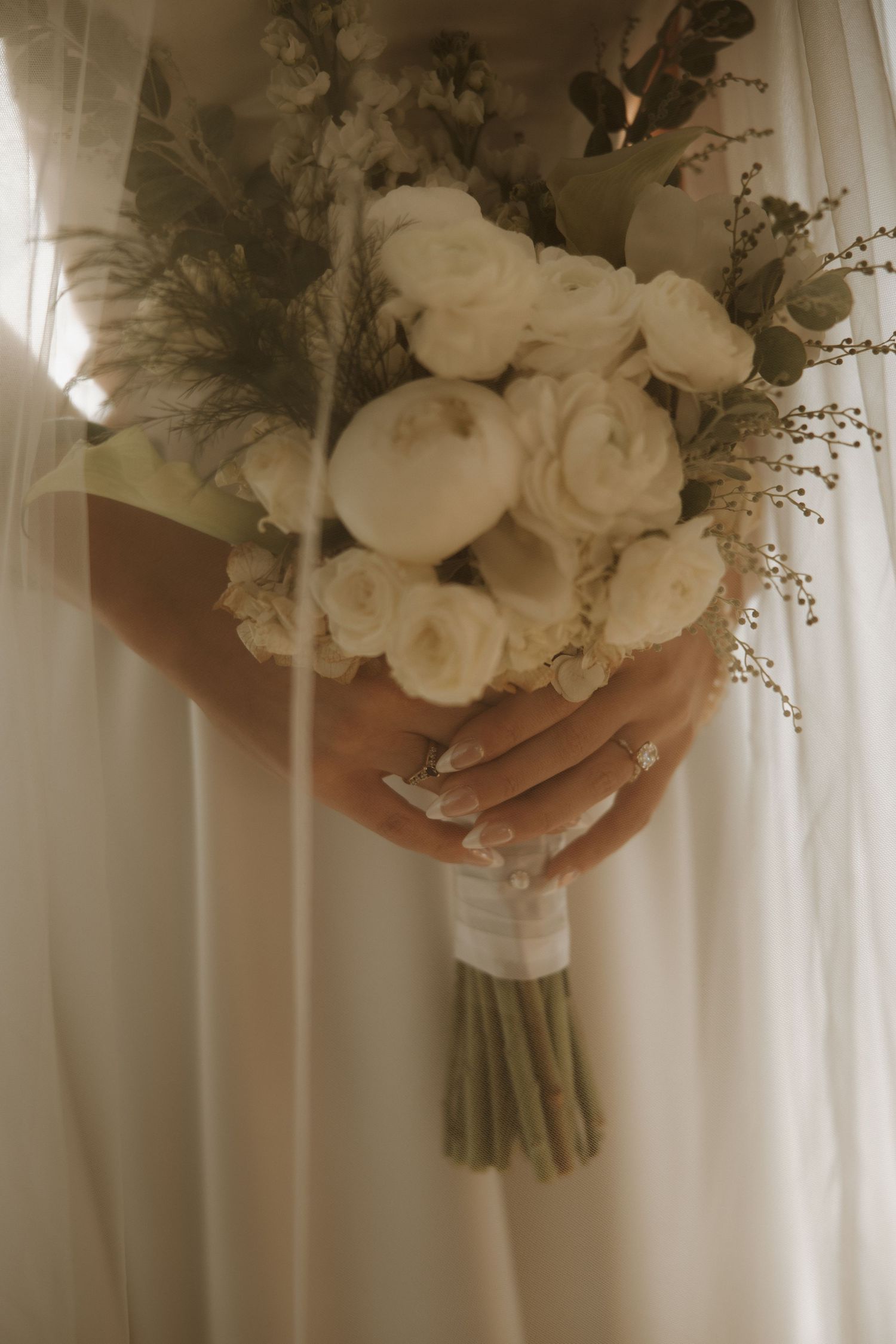 Close-up view of elegant white rose wedding bouquet held against a flowing white dress.
