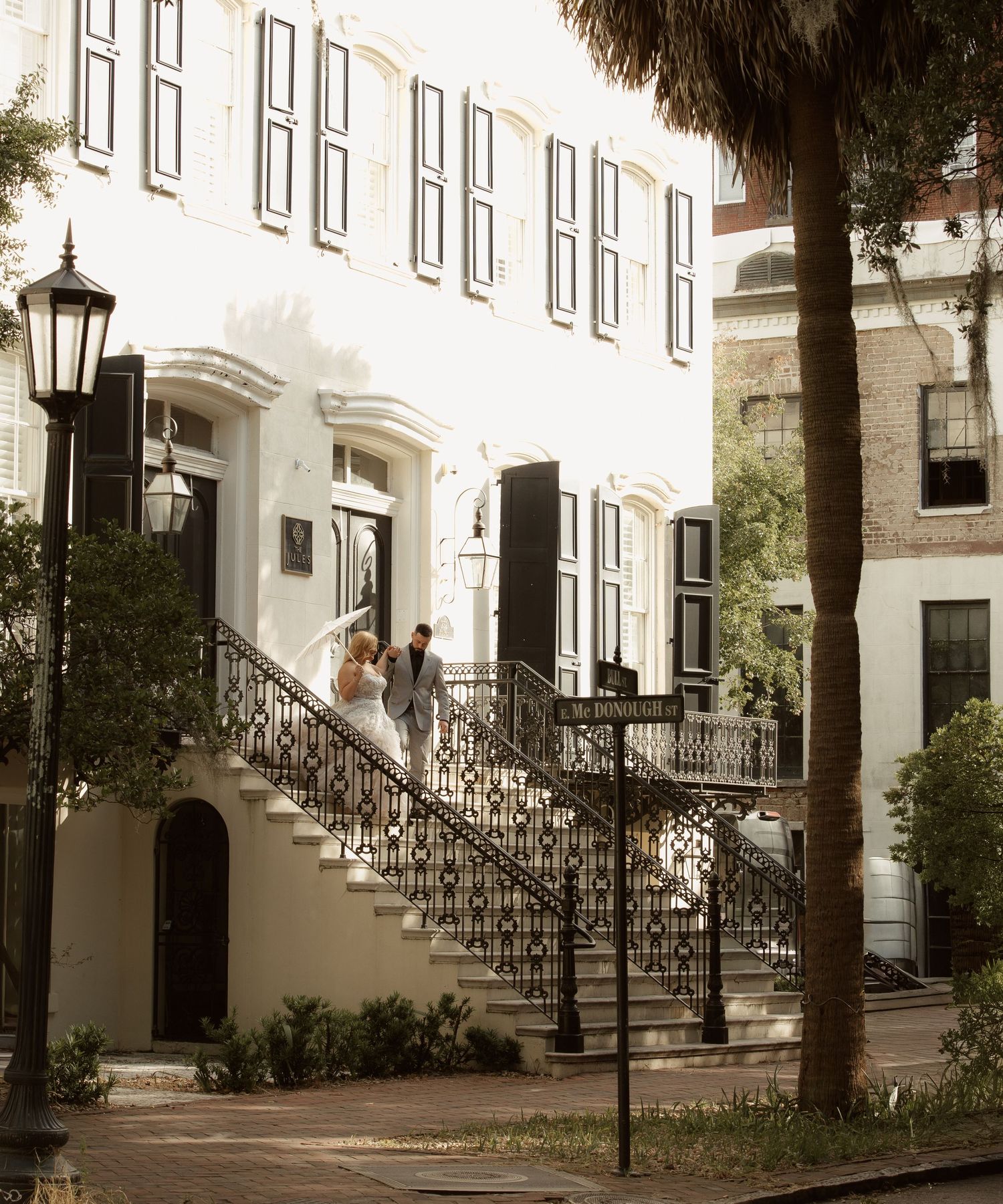 Historic row of white townhouses with ornate iron railings and stairs along a tree-lined street in Charleston, South Carolina.
