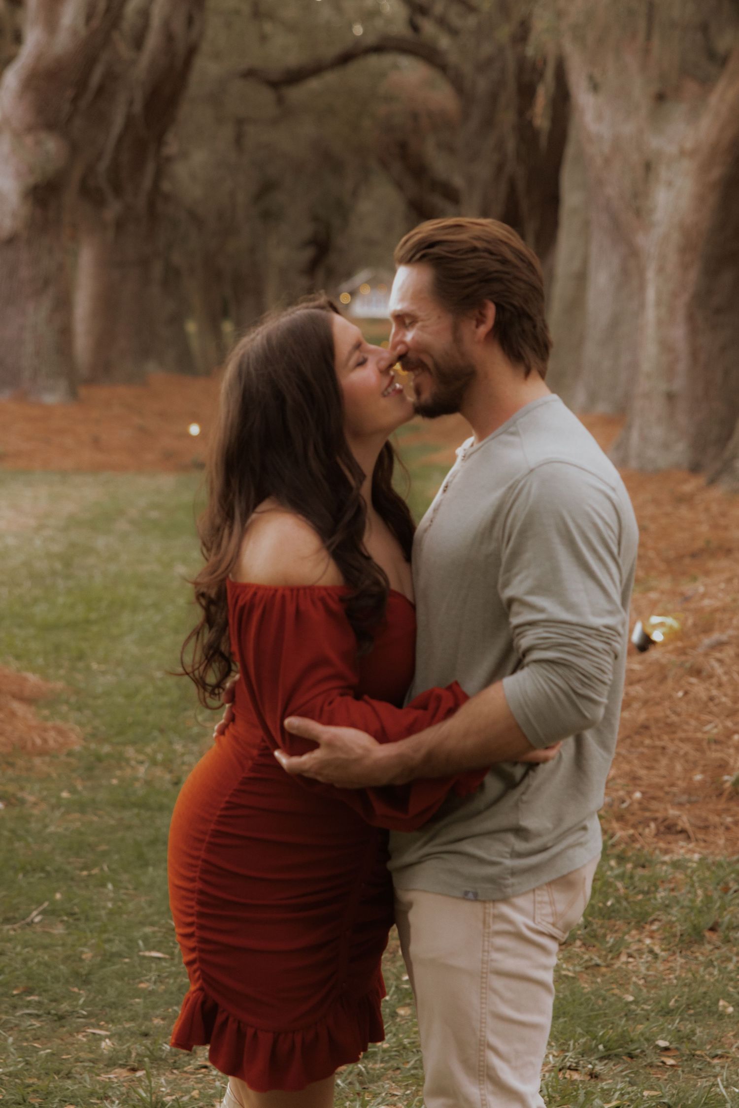 Romantic couple sharing an intimate moment in a rustic outdoor setting with tall trees in the background.