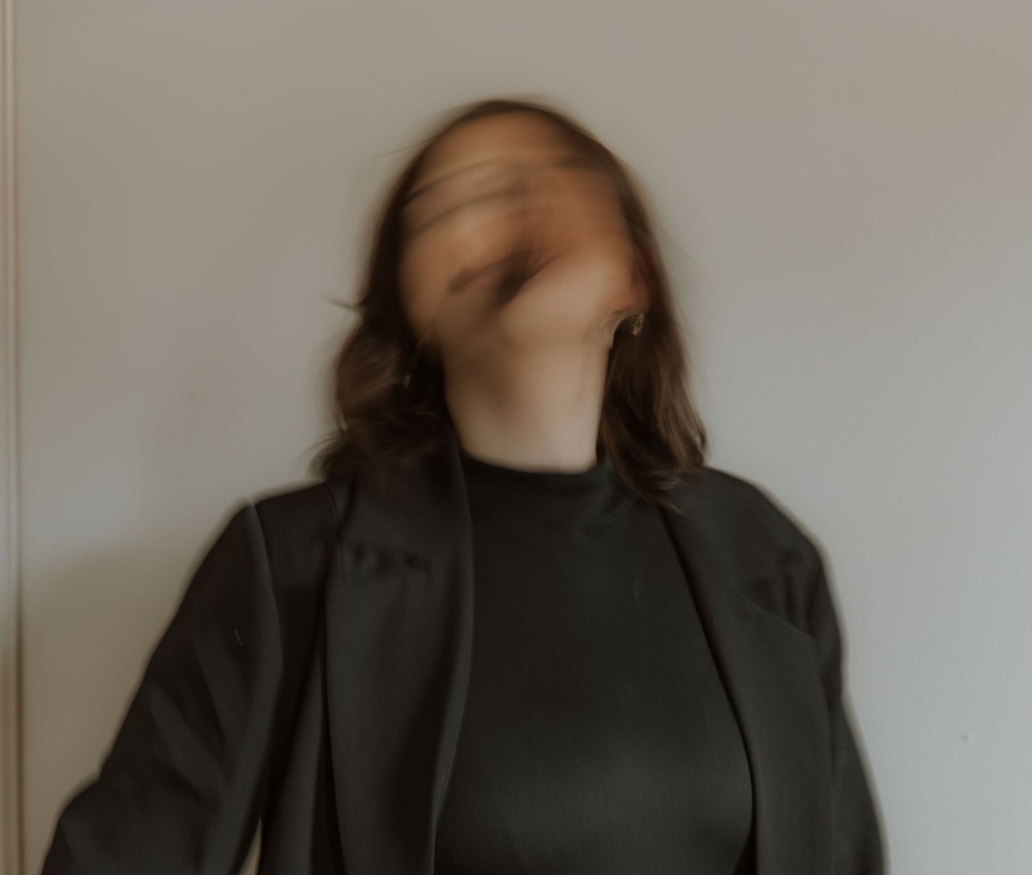 Artistic motion blur portrait in black turtleneck against neutral wall.